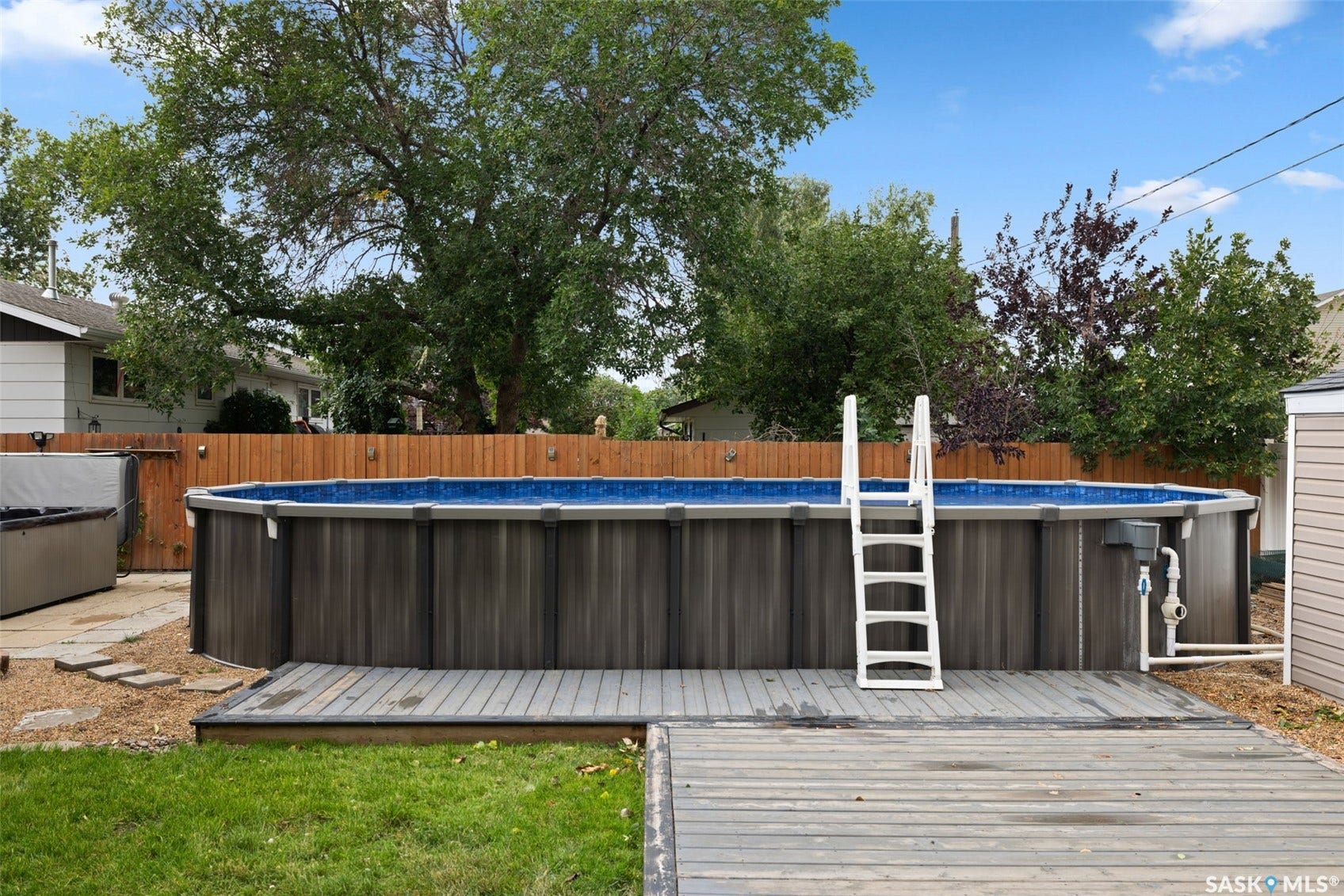 Above-ground swimming pool with an attached deck, wood-finish siding, and a white access ladder