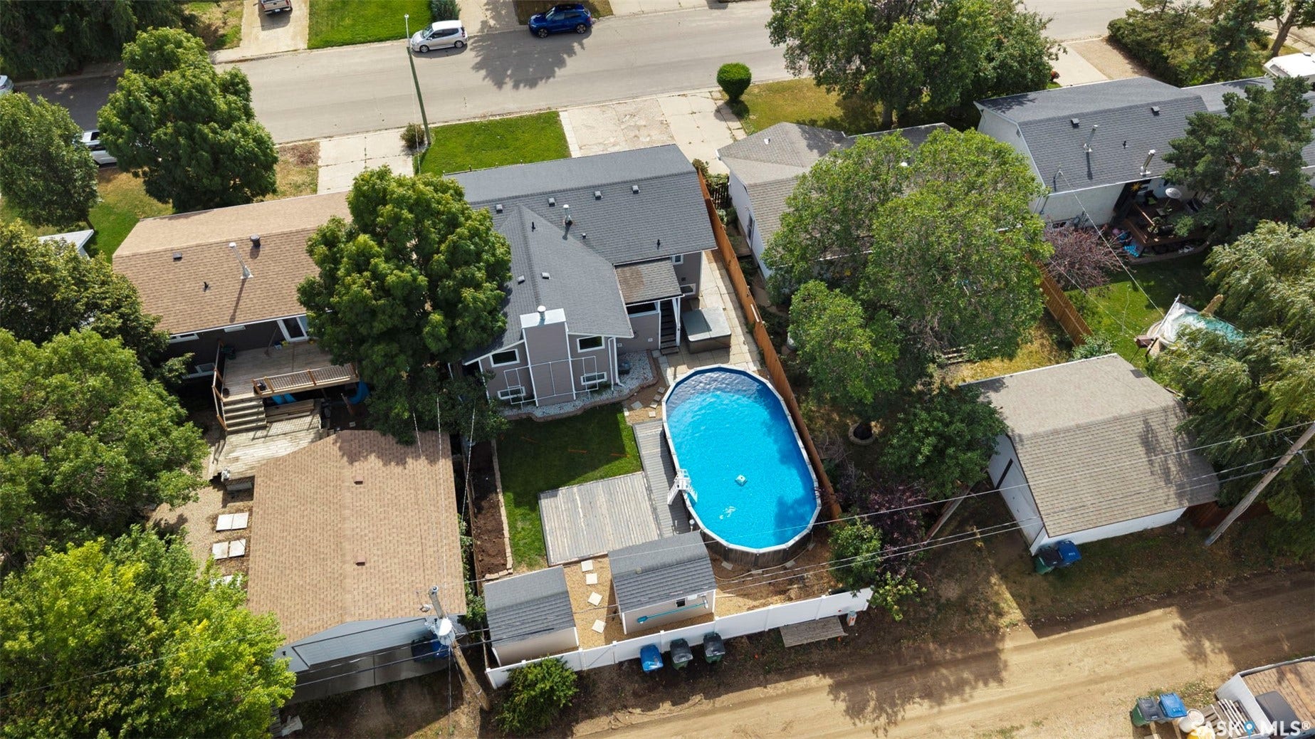 Property featuring a dark shingle roof, a backyard with an above-ground pool, and mature trees