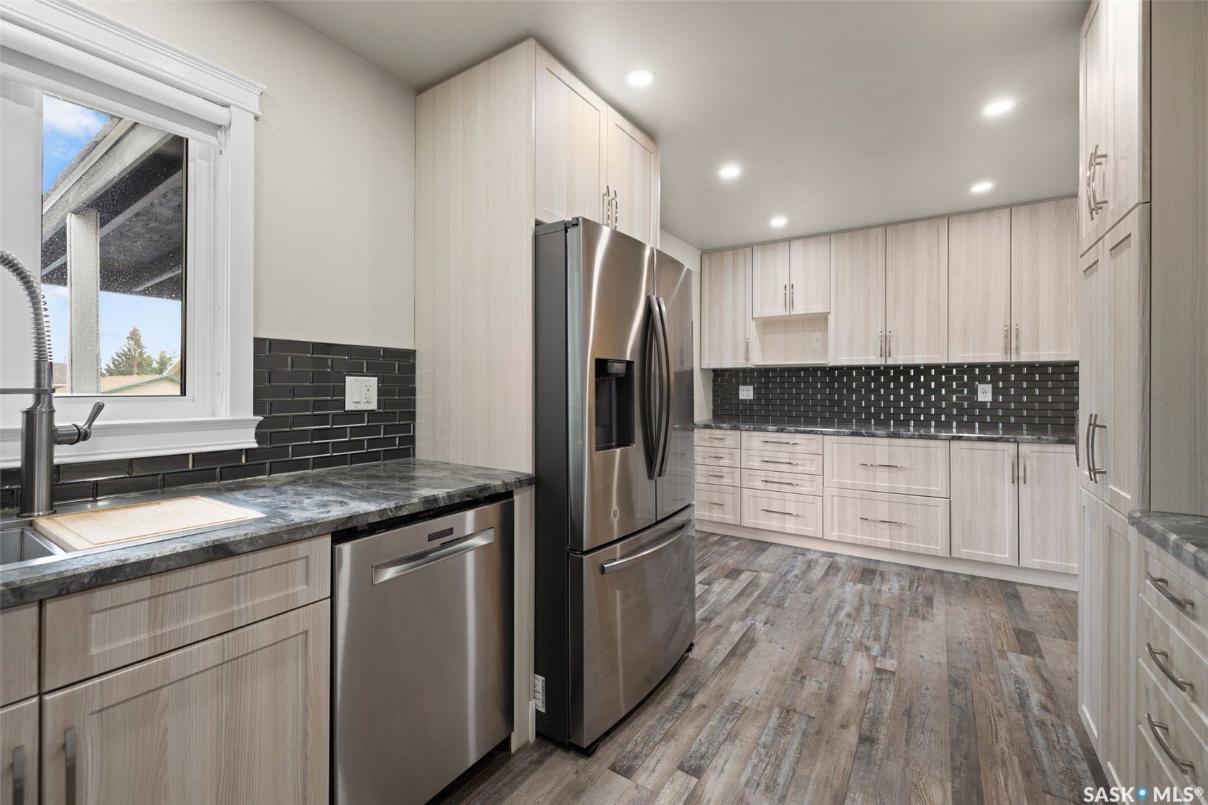 Stainless steel refrigerator and dishwasher, wood-finish flooring, light wood-finish cabinetry, and dark subway tile backsplash
