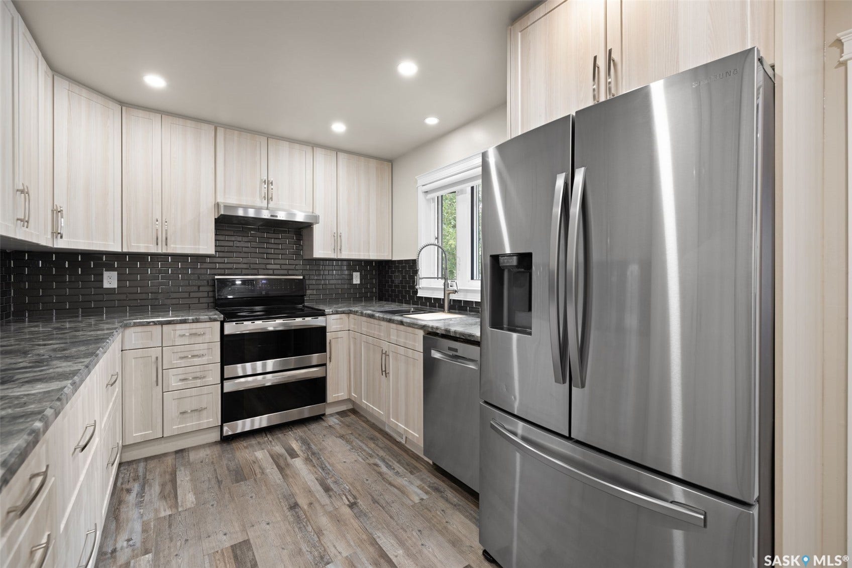 Kitchen featuring light wood-finish cabinetry, dark subway tile backsplash, stainless steel appliances, a double oven range, and wood-finish flooring