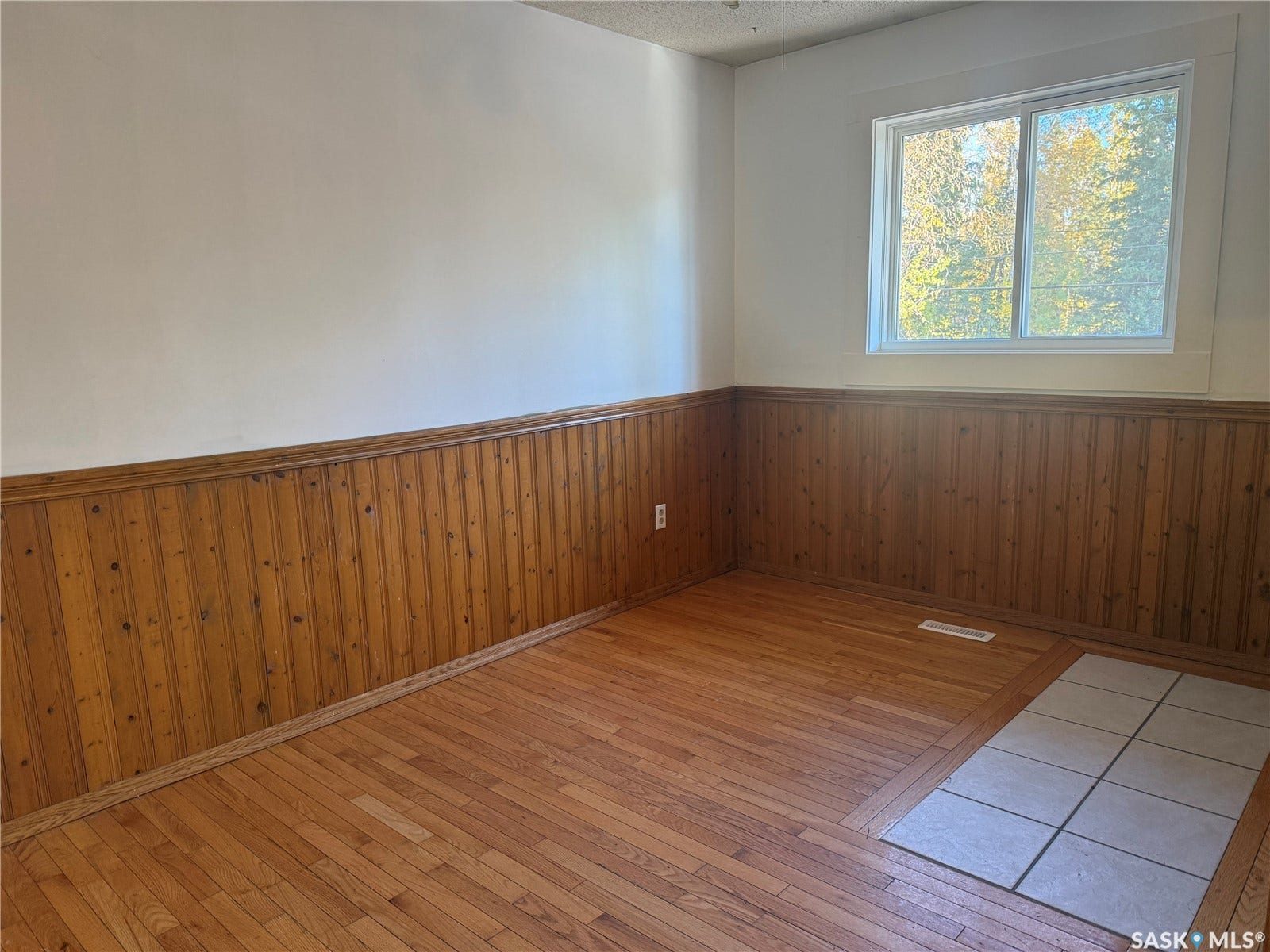 708 Studer Street, La Ronge SK S0J 1L0 Wood-finish flooring, wood paneling, white walls, and a white window frame