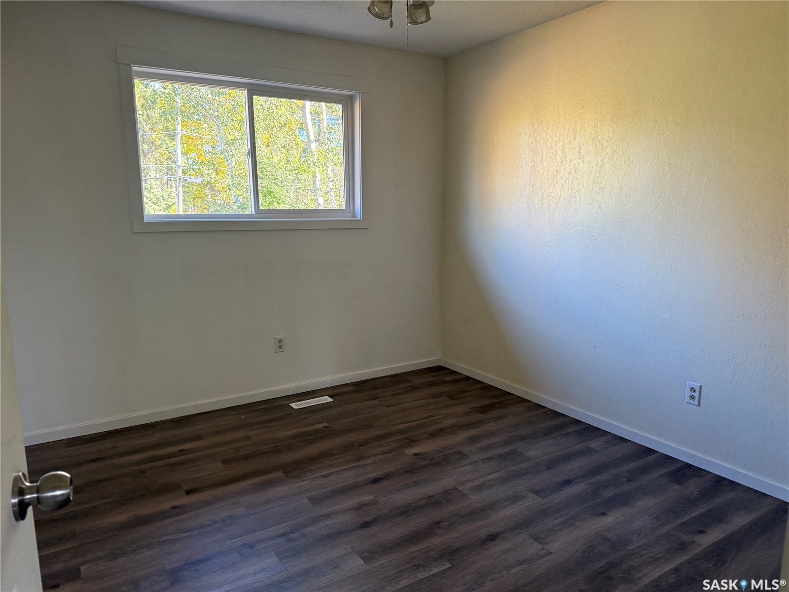 708 Studer Street, La Ronge SK S0J 1L0 Wood-finish flooring with a neutral wall color, featuring a sliding window and a ceiling-mounted light fixture