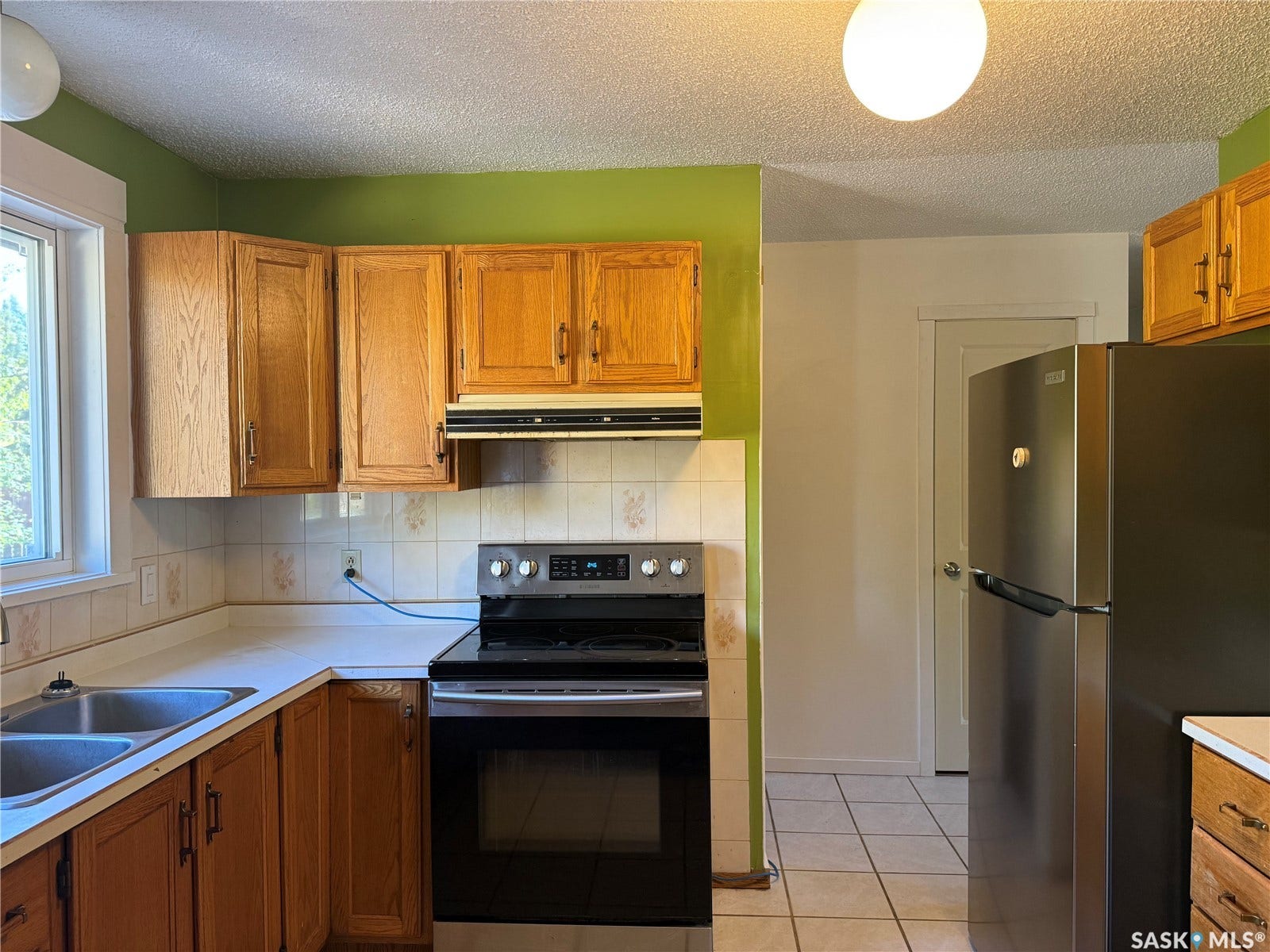 708 Studer Street, La Ronge SK S0J 1L0 Kitchen featuring wood cabinetry, stainless steel range, stainless steel refrigerator, dual basin sink, and tiled flooring