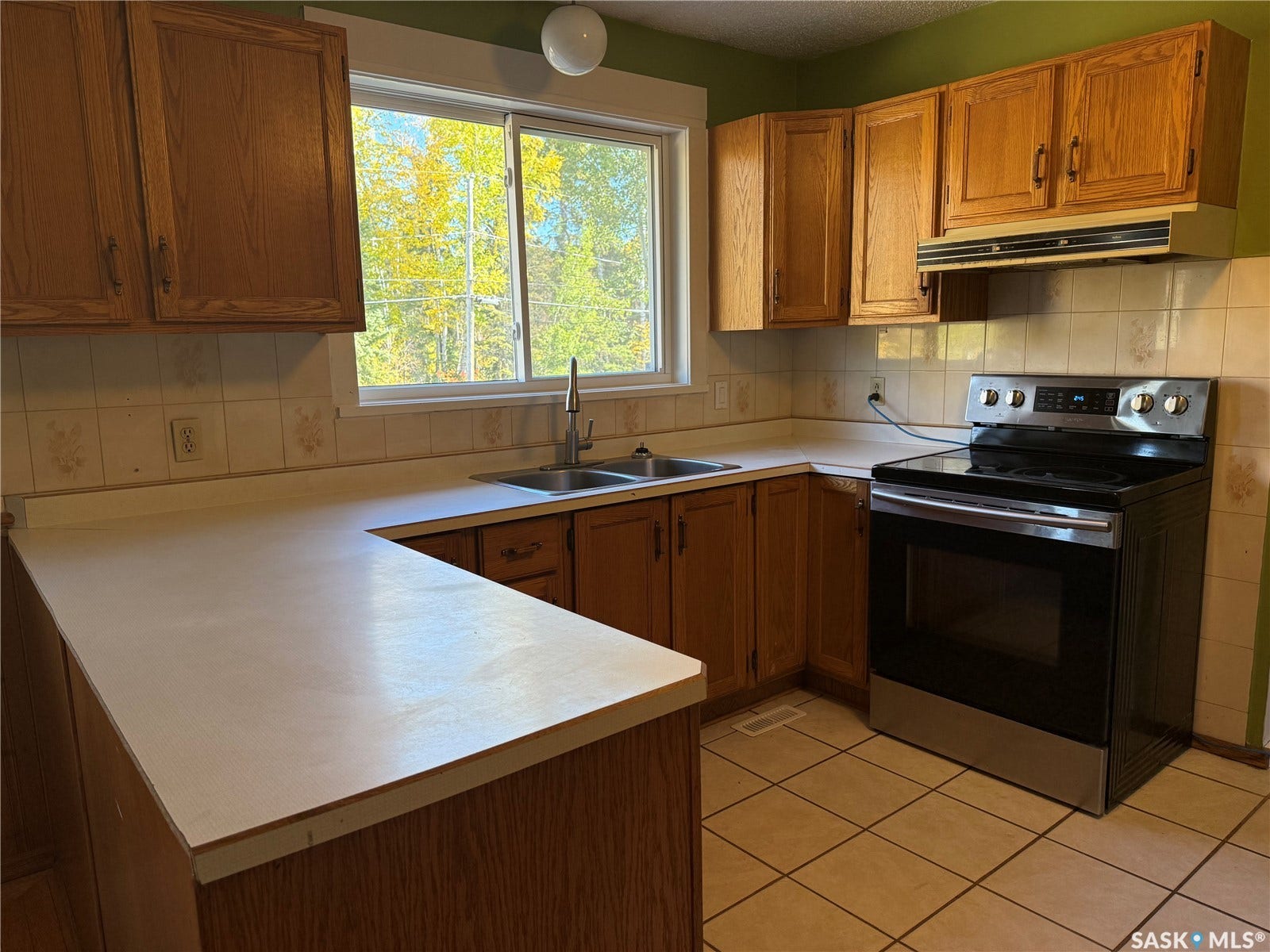 708 Studer Street, La Ronge SK S0J 1L0 U-shaped laminate countertop, stainless steel electric range, wood cabinetry, tile backsplash, and tile flooring