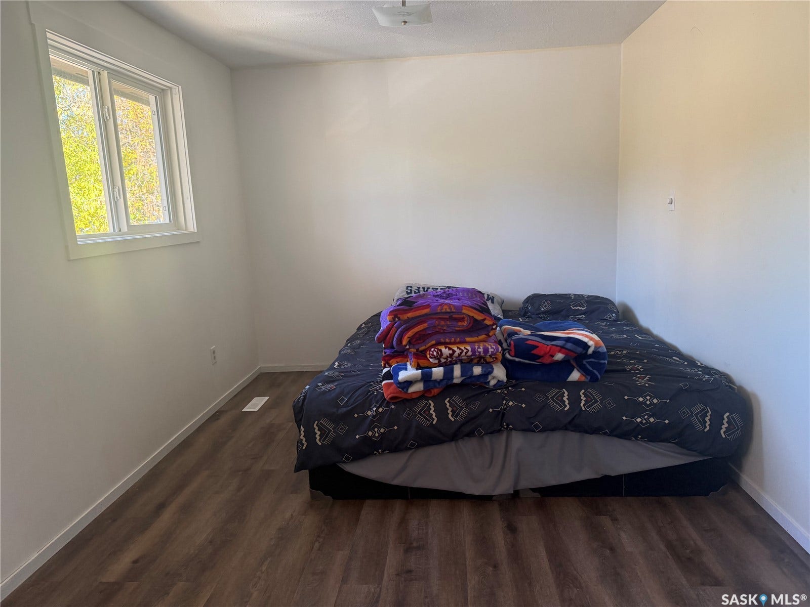 708 Studer Street, La Ronge SK S0J 1L0 Wood-finish flooring, white walls, and a window with white trim