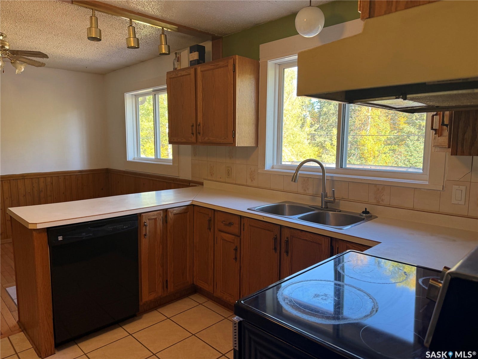 708 Studer Street, La Ronge SK S0J 1L0 Kitchen featuring wood cabinetry, a double basin stainless steel sink, a black built-in dishwasher, and a black electric range with a cooktop