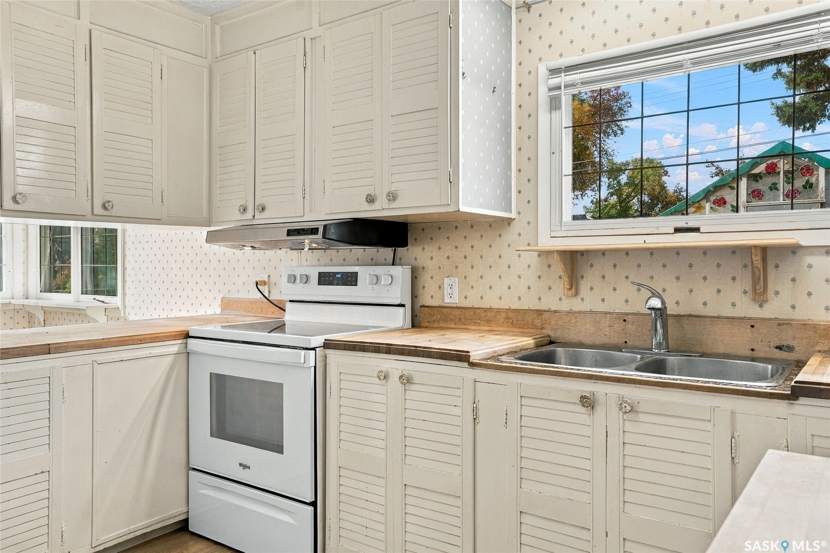 White shutter-style cabinetry, wood-finish countertops, and a double basin stainless steel sink