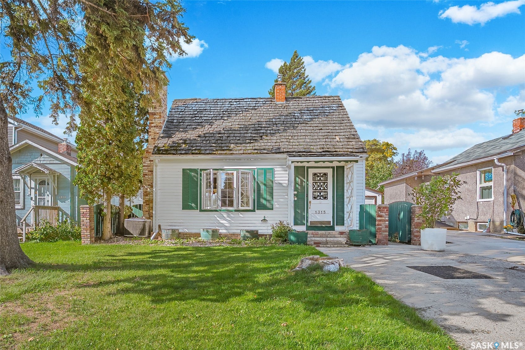White siding exterior with green window shutters, a front entry porch, and a brick chimney