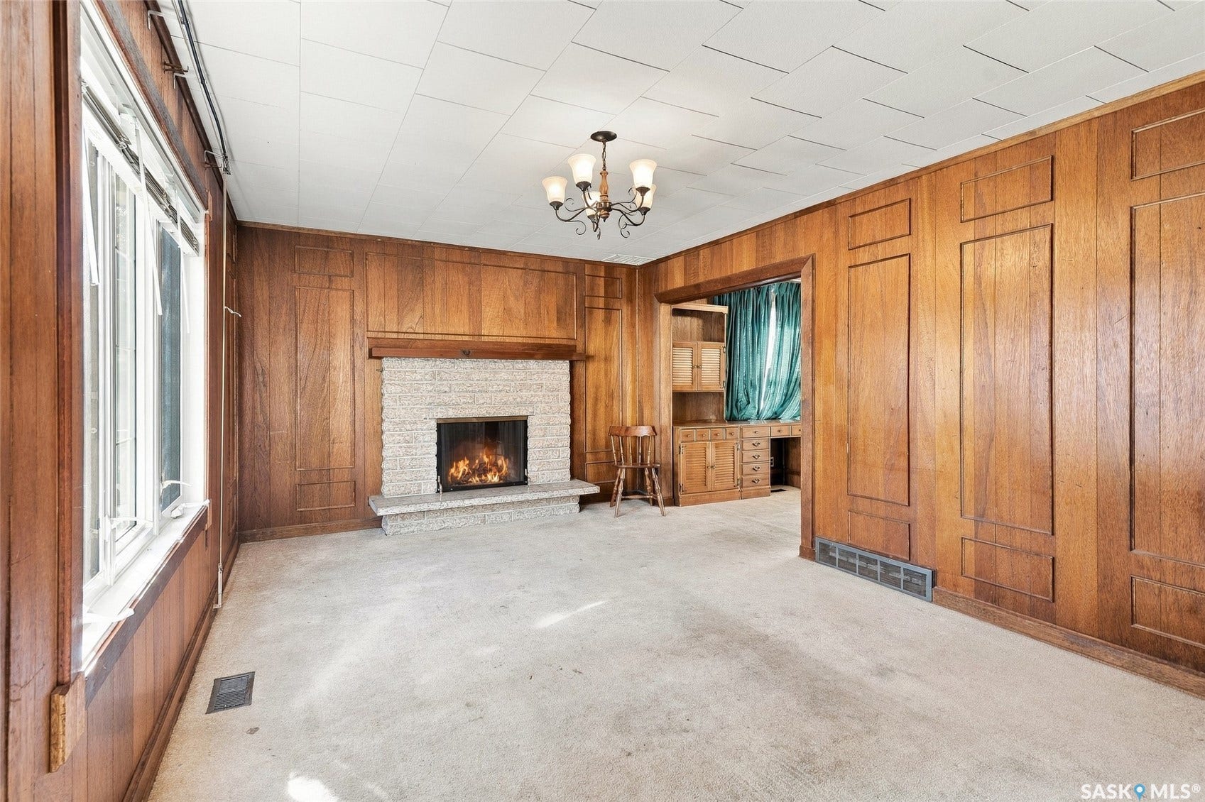 Wood paneled walls, stone-clad fireplace with wood mantle, multi-pane windows, decorative ceiling panels, built-in cabinetry