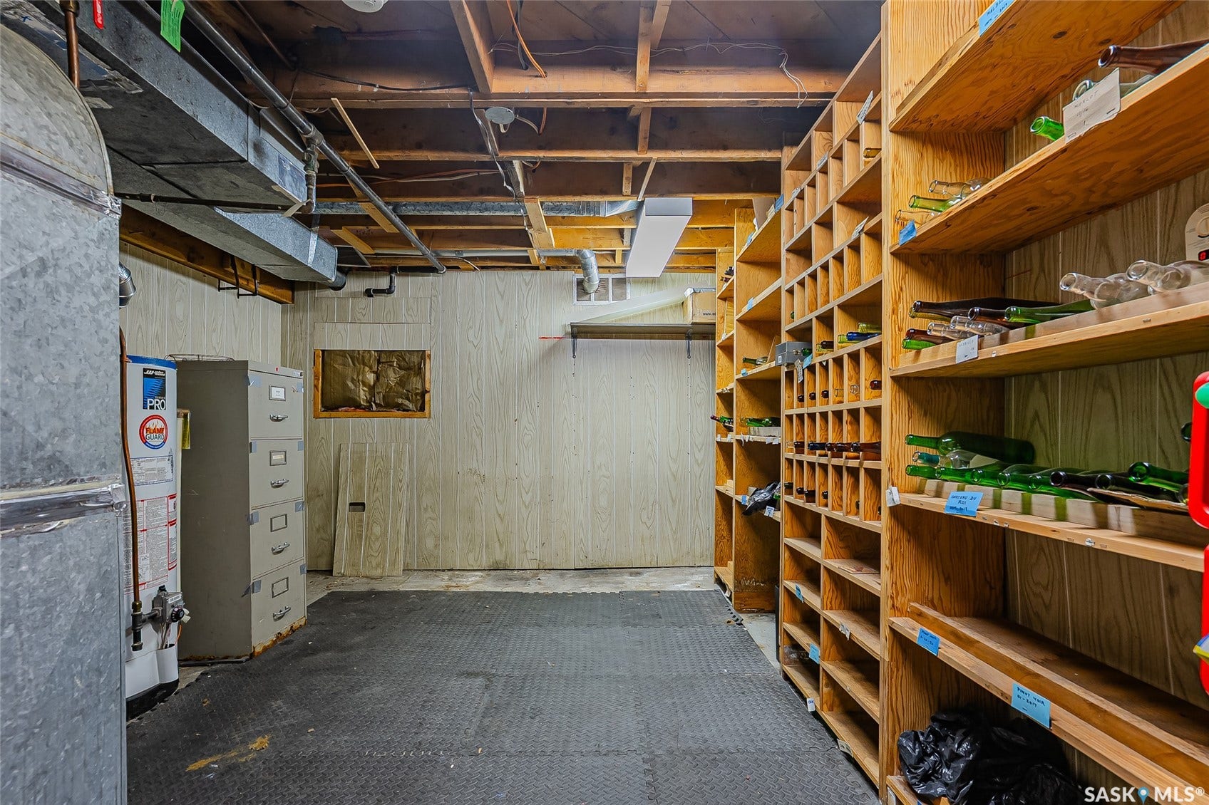 Unfinished basement featuring exposed ceiling joists and ductwork, wood-paneled walls, utility water heater, and extensive built-in wooden shelving
