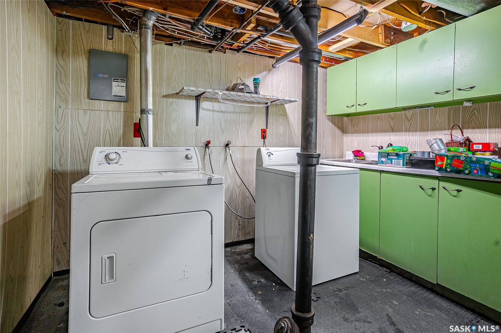Laundry area featuring a washer and dryer, exposed ceiling joists, wood-look paneling, and built-in green cabinetry with an integrated sink
