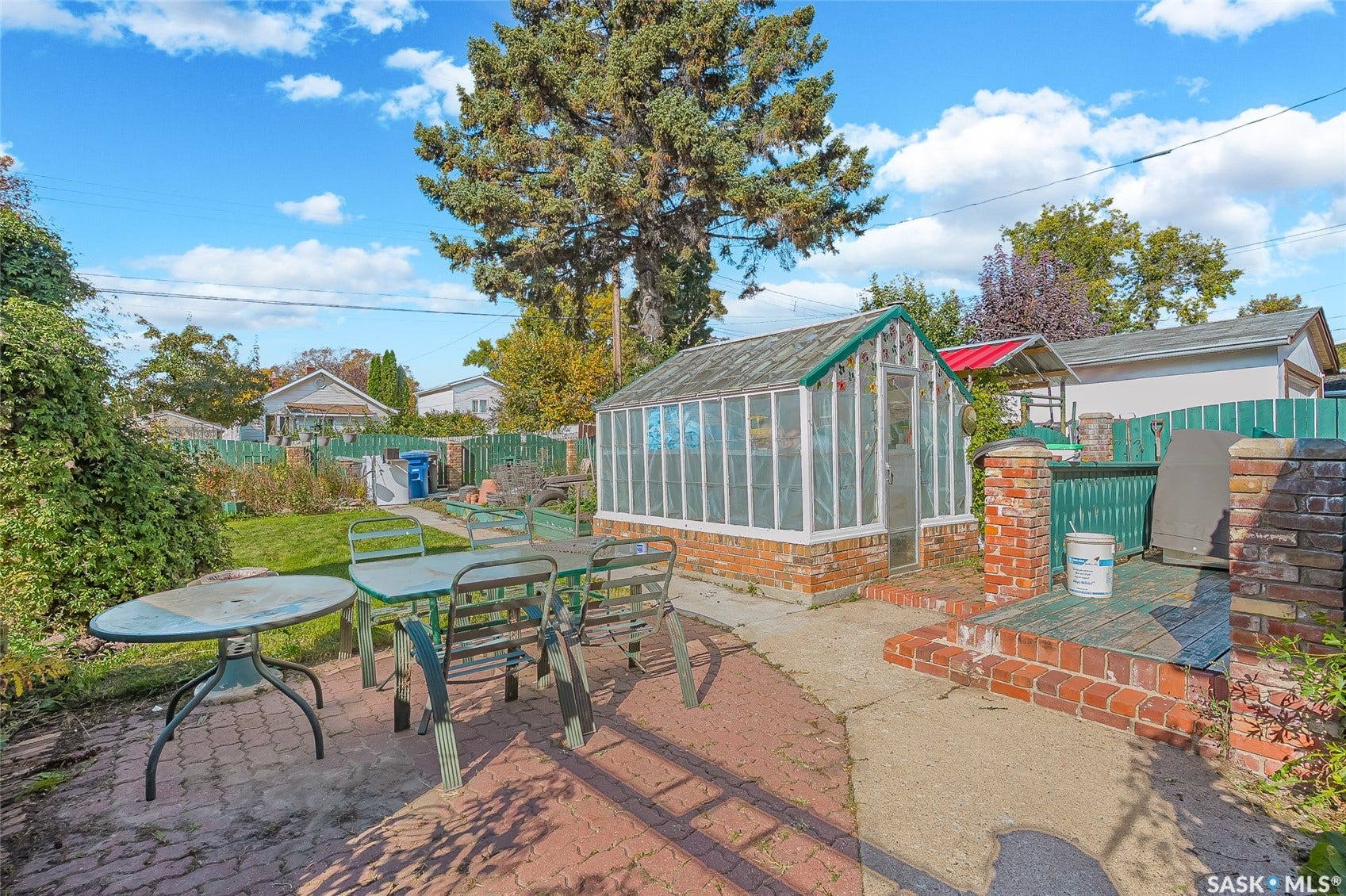 Expansive backyard featuring a manicured lawn, a red brick patio, a built-in greenhouse, and a wooden fence
