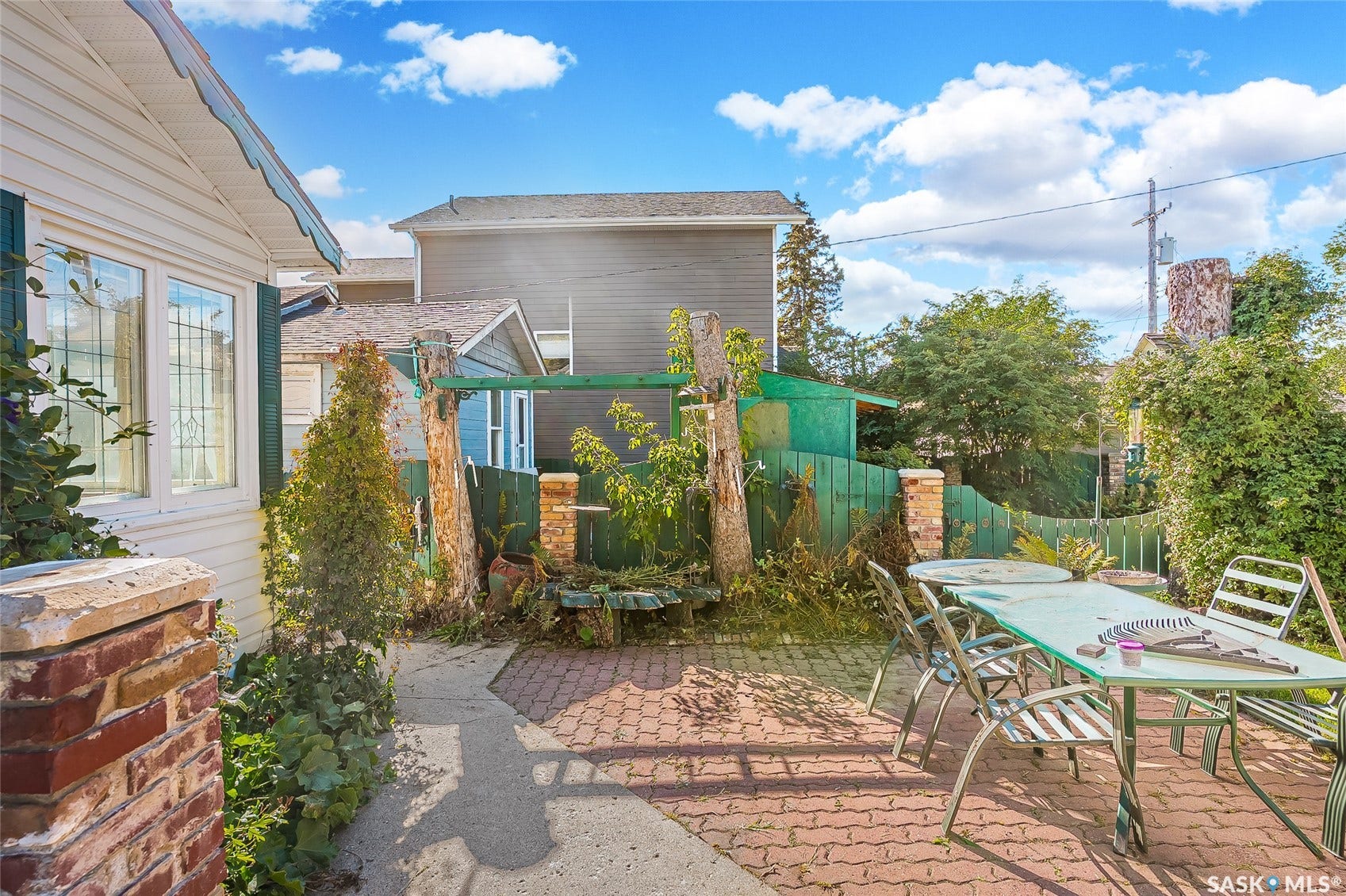 Patio with brick paver flooring and an exterior wall featuring white siding and green shutters