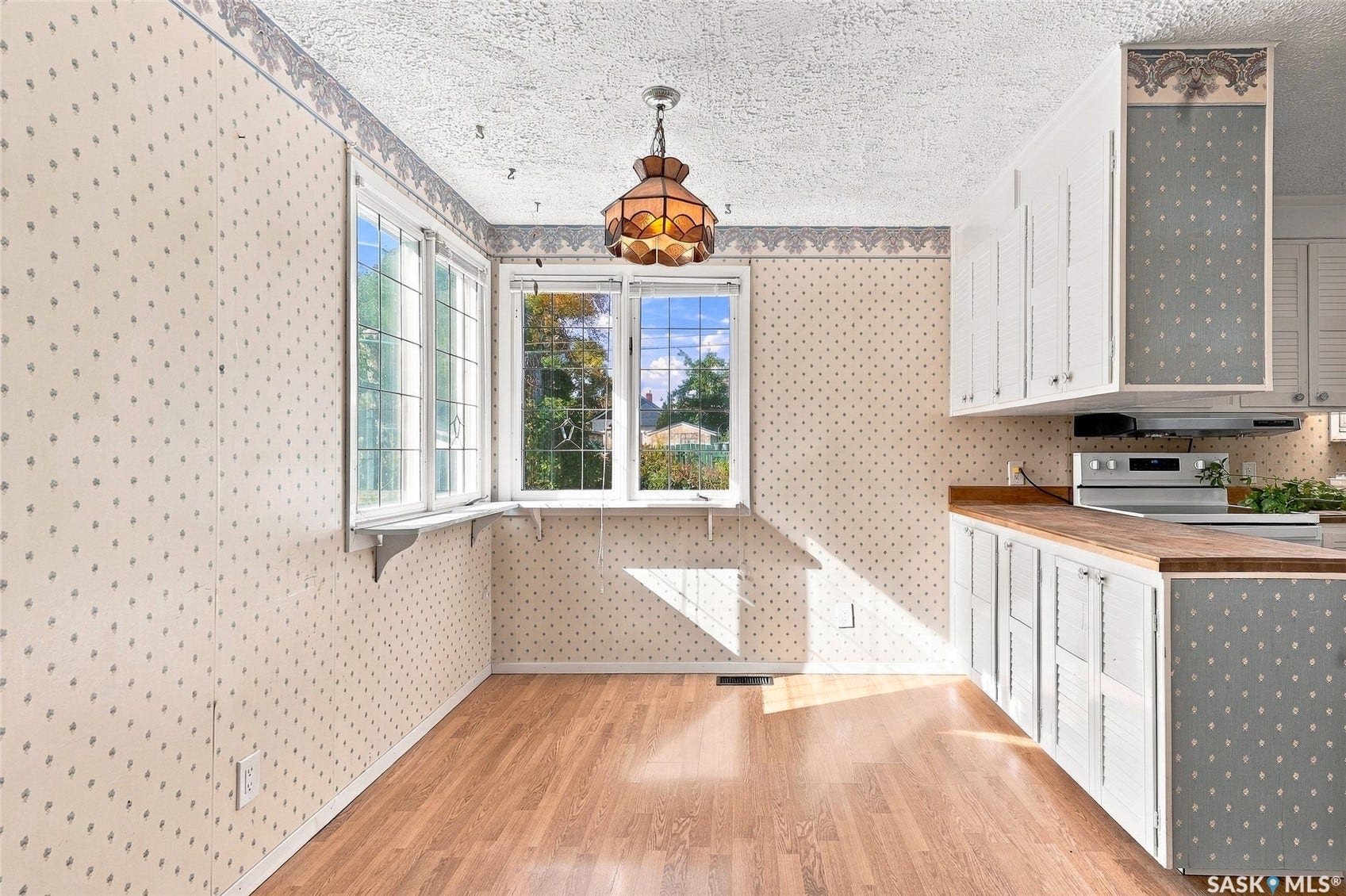 Wood-finish flooring, white cabinetry with patterned panels, built-in wall oven, and a decorative pendant light fixture