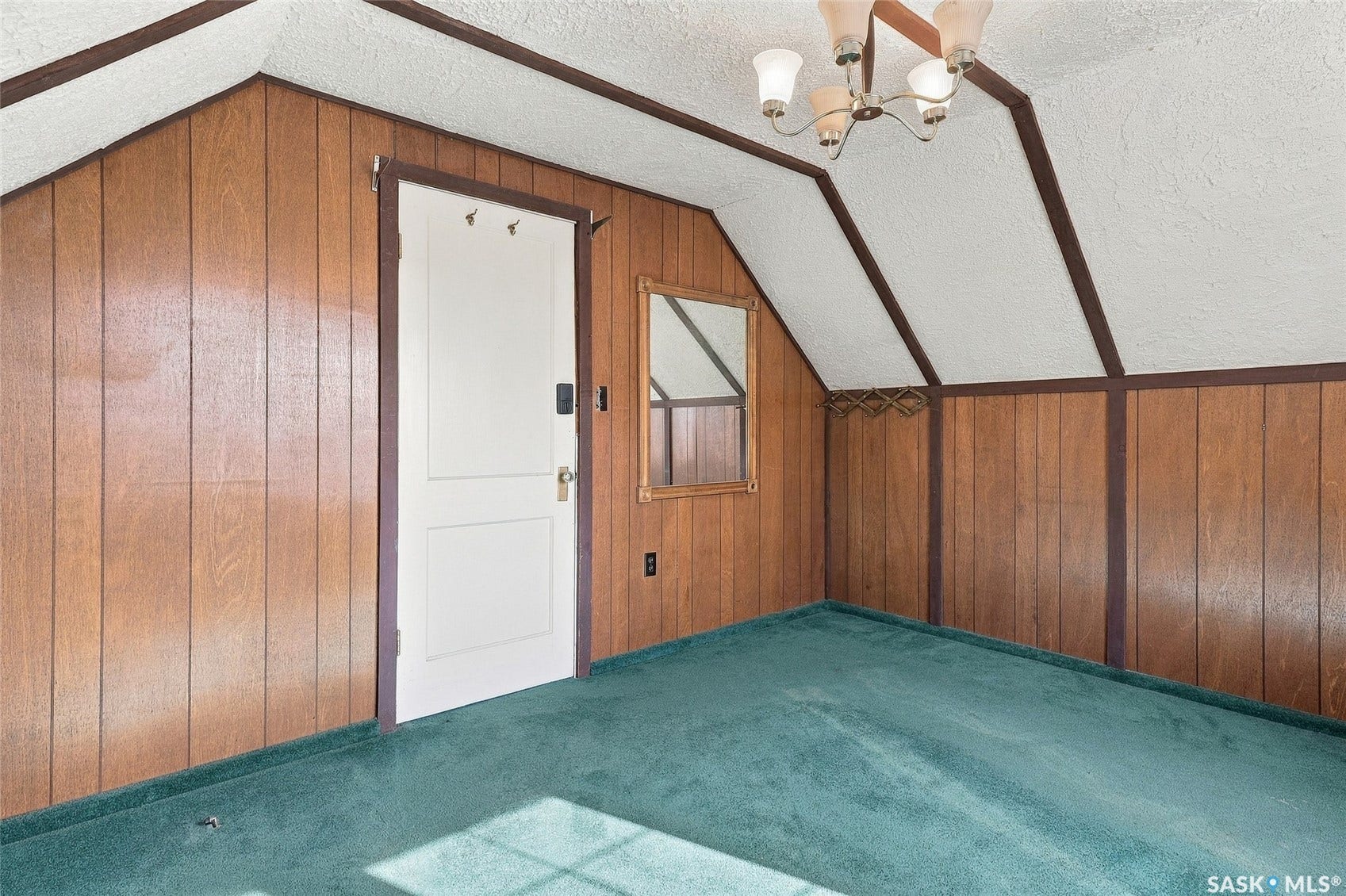 Sloped ceiling, wood paneling, paneled door, wall-mounted light fixture, and carpet flooring