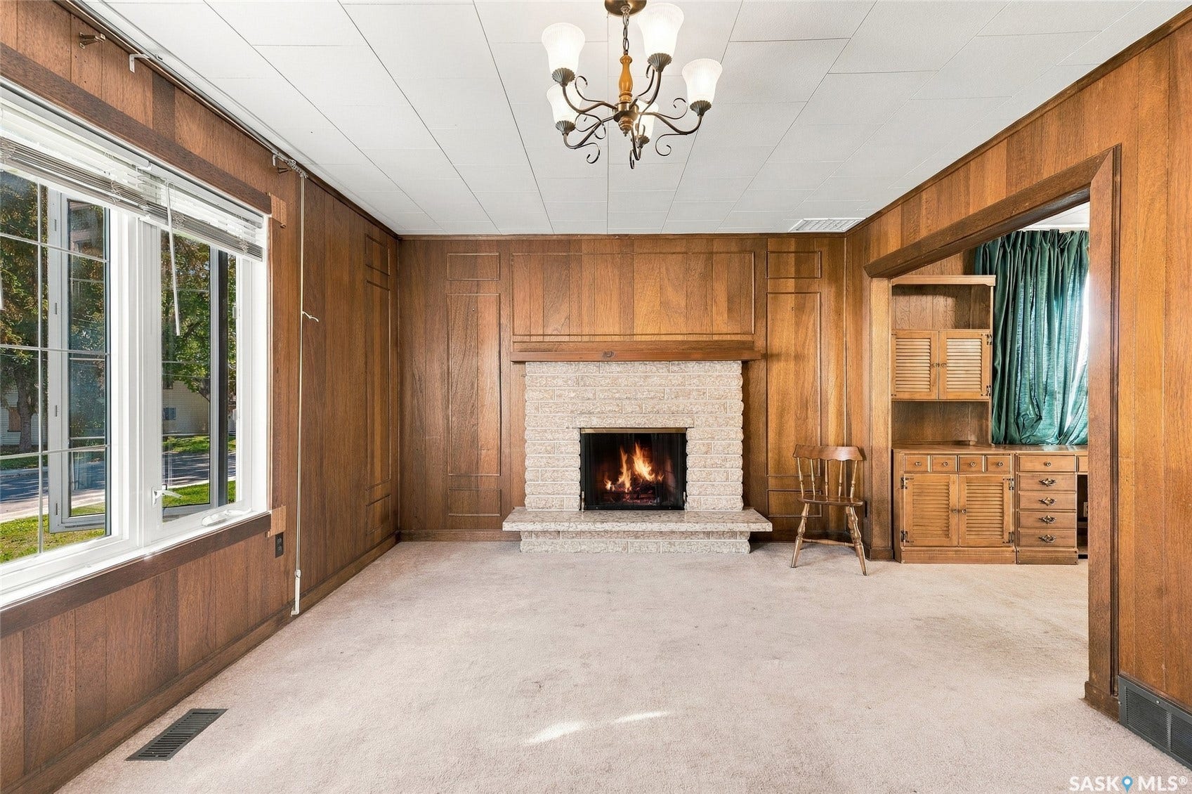 Wood-paneled walls with decorative trim, stone-clad fireplace, built-in cabinetry, and a multi-pane window