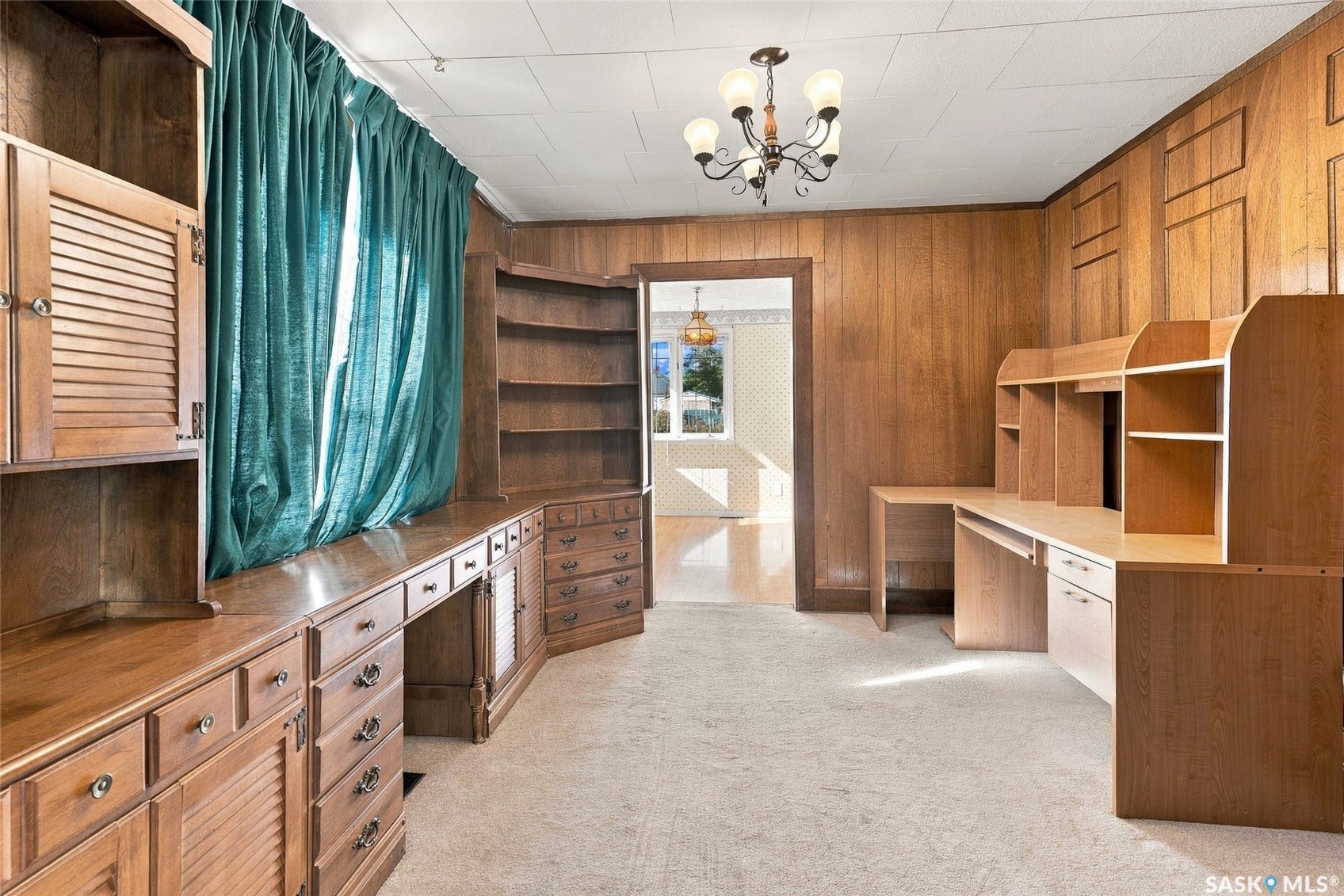 Room featuring extensive wood paneling, built-in desk units, integrated shelving, and a decorative ceiling fixture