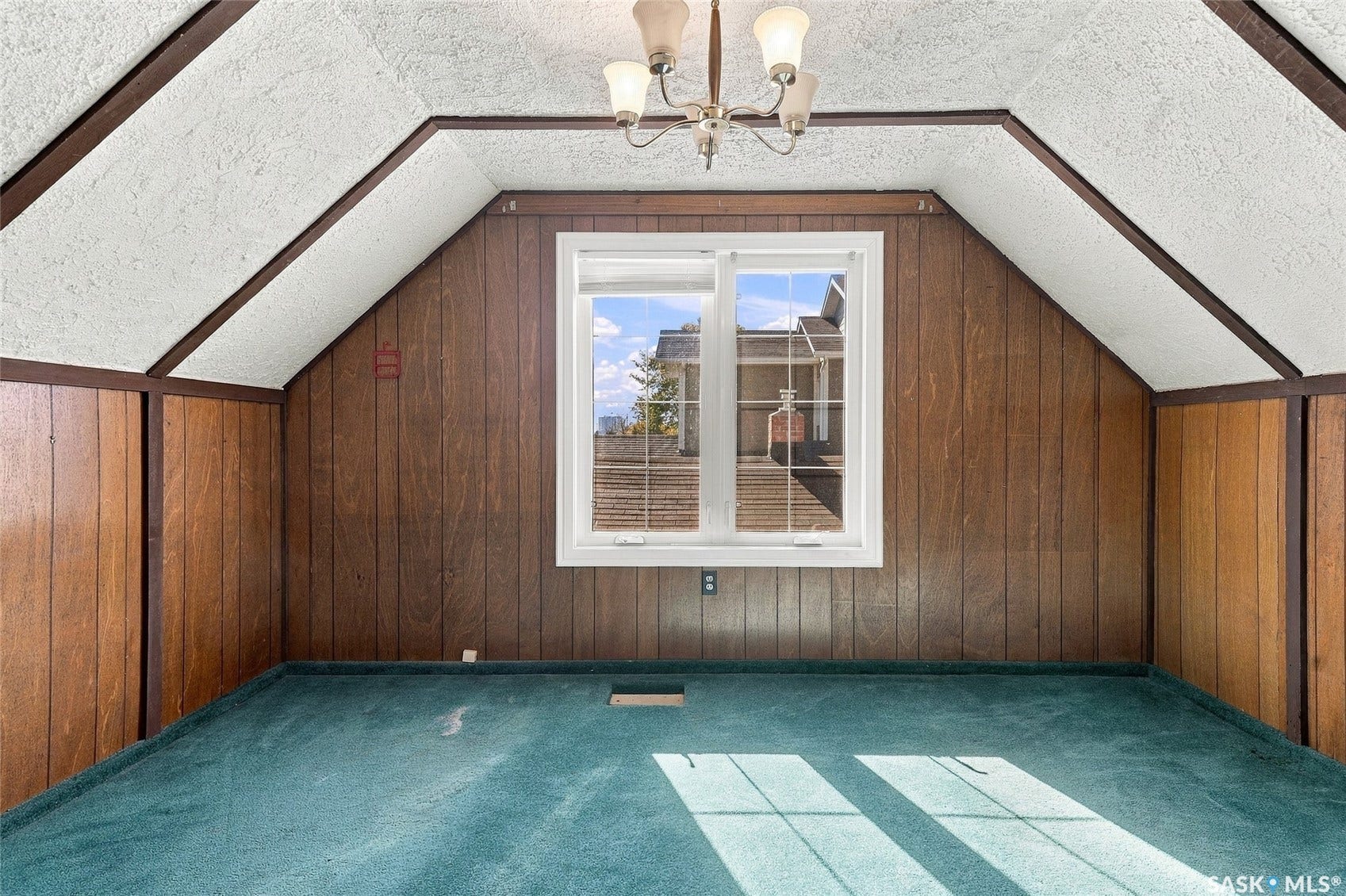 Sloped ceiling with exposed beams, wood-paneled walls, and a central window