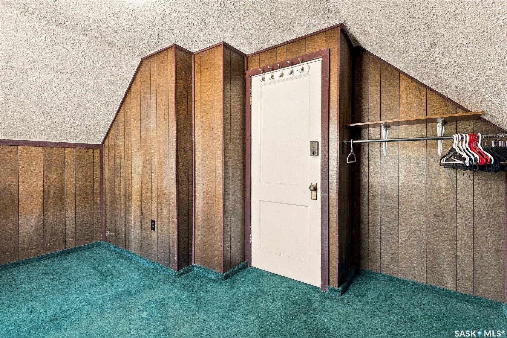 Wood-paneled walls with sloped ceiling, teal carpet, and built-in garment rack
