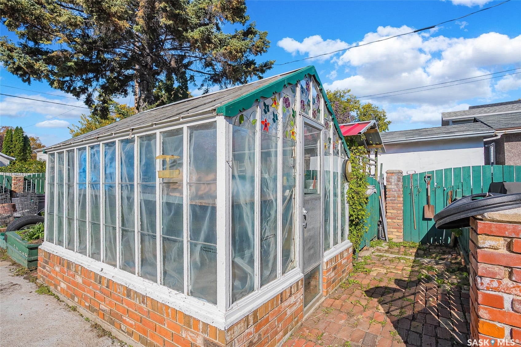 Brick foundation greenhouse with a shingled roof, glass panel walls, and a brick paver pathway