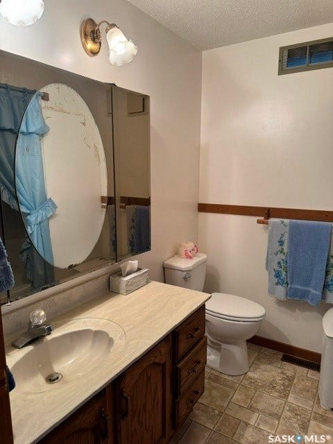 Bathroom featuring a vanity with an integrated sink, medicine cabinet, wall-mounted lighting, and a toilet