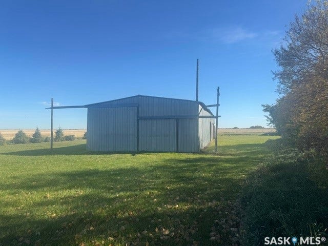 Metal-sided outbuilding with a blue metal roof, set on a grassy expanse
