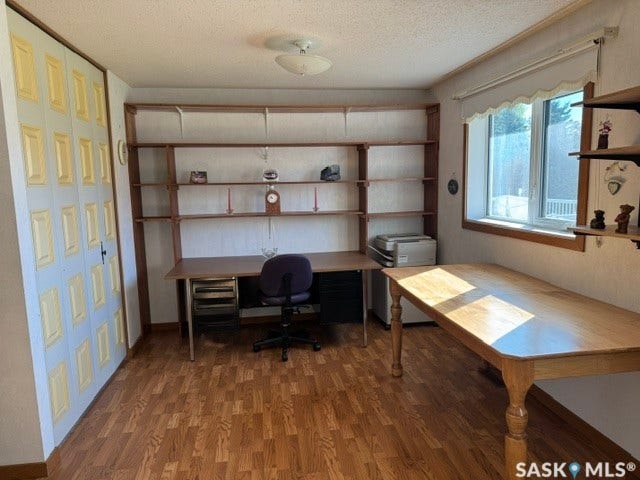 Wood-finish flooring throughout, featuring a built-in wood shelving unit, a desk area with integrated storage, and a window with a roller shade