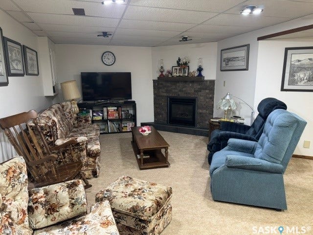 Carpeted room featuring a built-in fireplace with stone-look surround and hearth, recessed ceiling lighting, and a drop ceiling