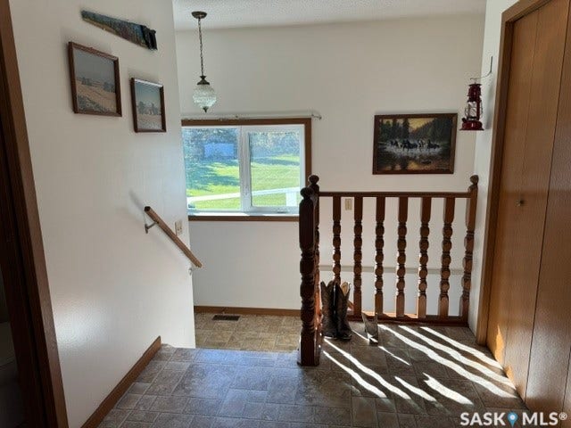 Entryway featuring a wood handrail, spindle railing, and a window with a green outdoor backdrop
