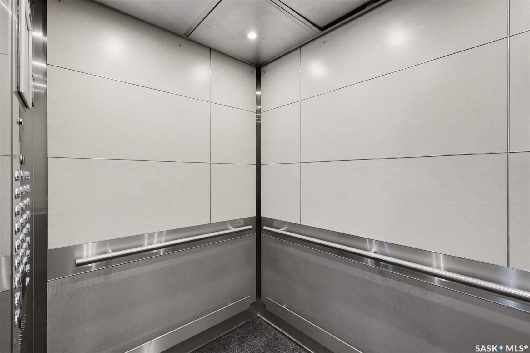 Interior elevator featuring light-toned wall panels, brushed metal accents, and a built-in handrail