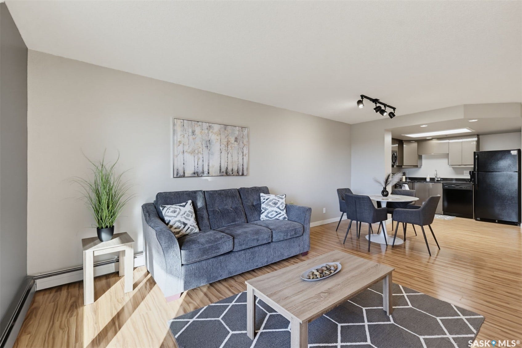 Open concept living area featuring wood-finish flooring, track lighting, and a kitchen with dark appliances