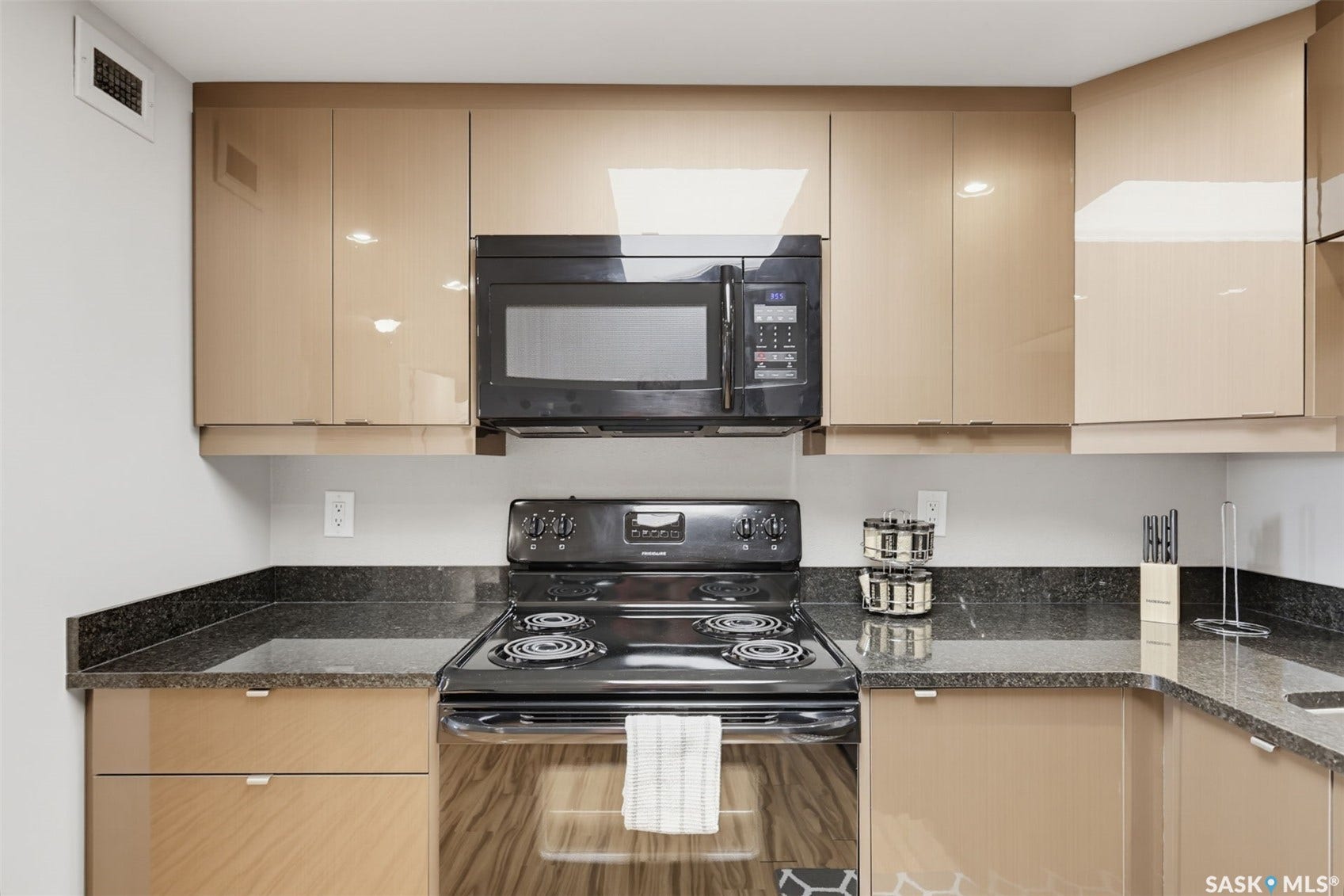 Kitchen featuring sleek cabinetry, dark countertops, built-in microwave, and black electric range