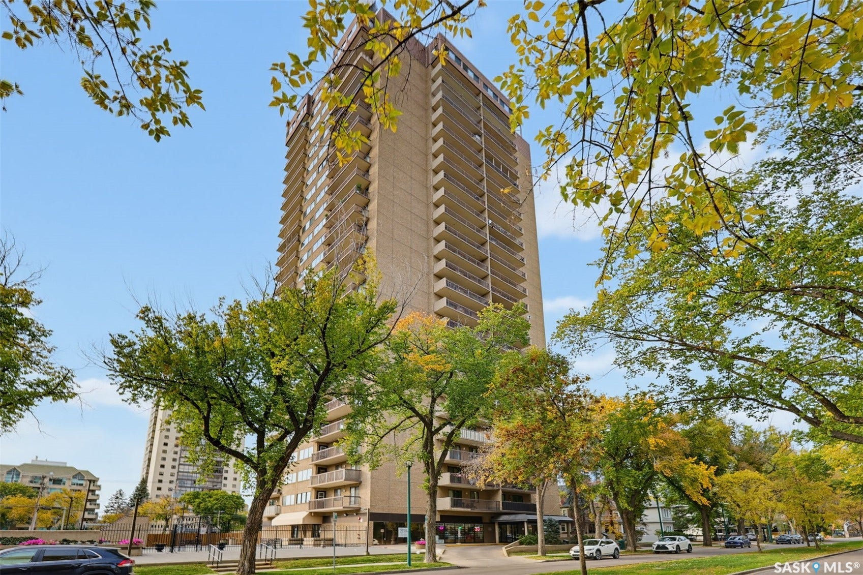 Multi-story building featuring numerous private balconies, a ground-level entrance with awnings, and surrounding mature trees