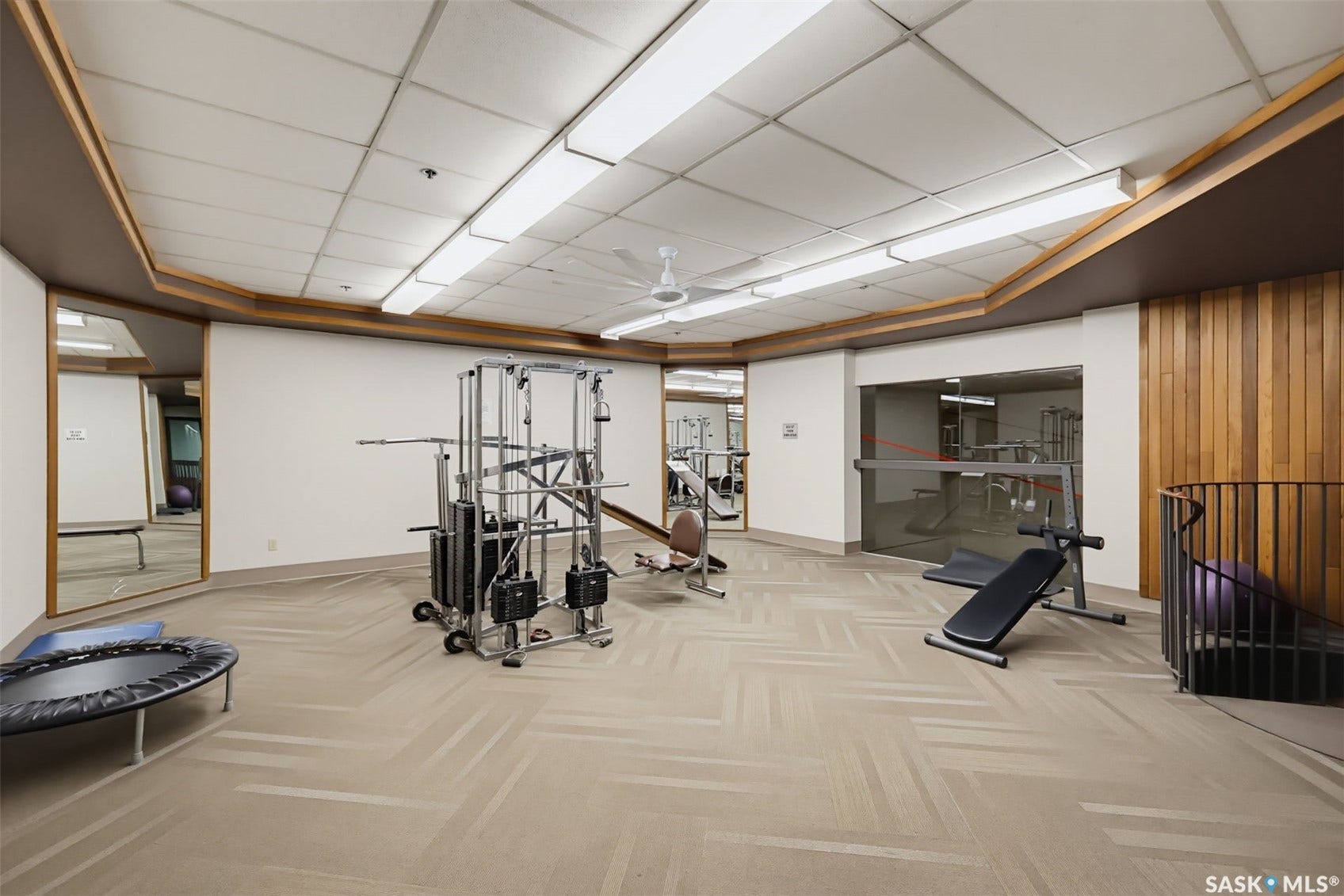 Fitness center with patterned carpet, wood wall paneling, and mirrored wall