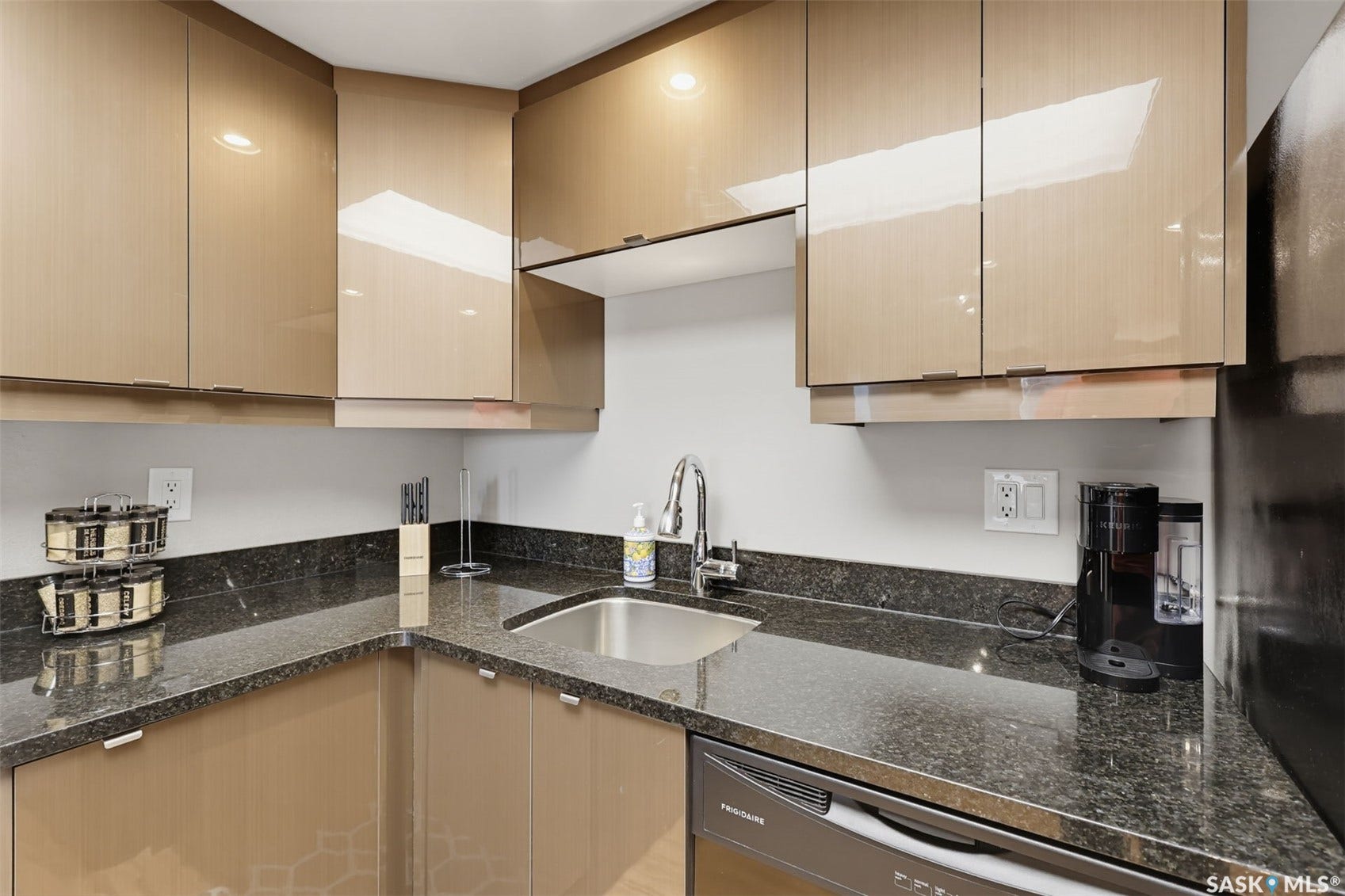 Sleek kitchen featuring dark speckled countertops, a stainless steel sink with a gooseneck faucet, light-colored upper and lower cabinetry, and a built-in dishwasher
