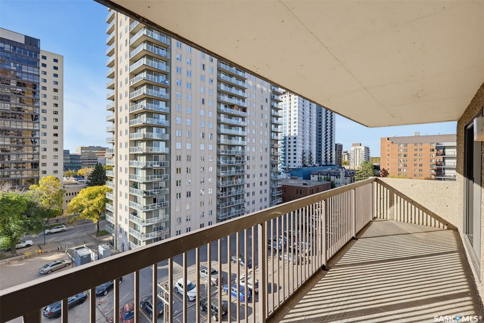 Private balcony with a metal railing, concrete flooring, and surrounding urban buildings