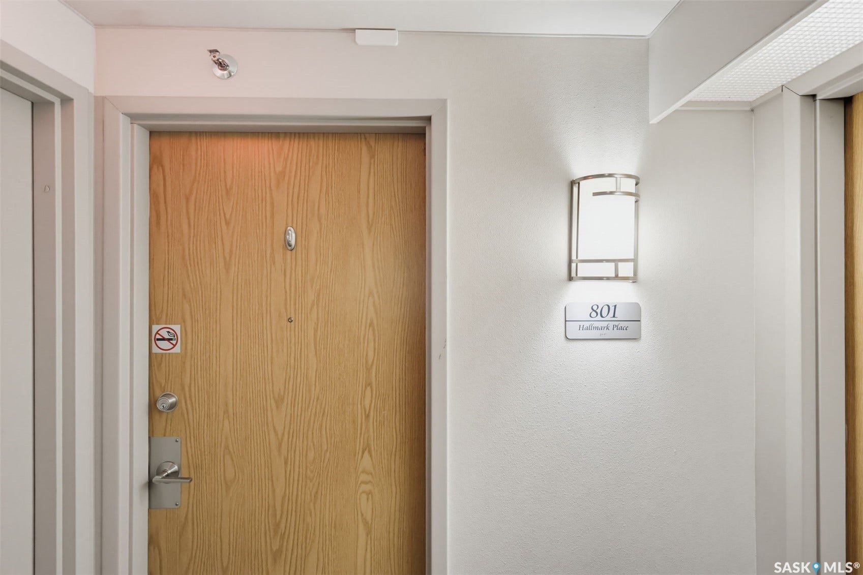 Entry door with wood-finish paneling, brushed nickel hardware, and an adjacent wall sconce