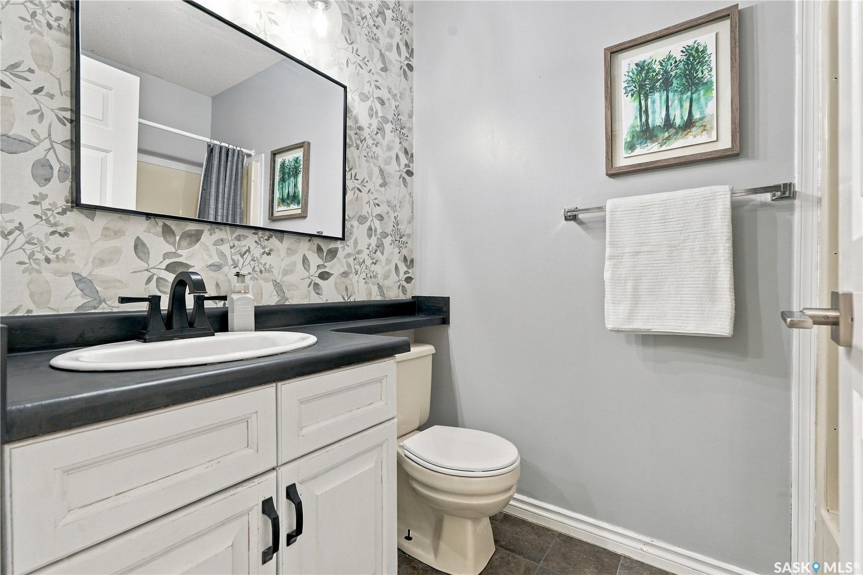 White vanity with black hardware and an integrated sink, dark countertop, black-framed mirror, and patterned accent wall
