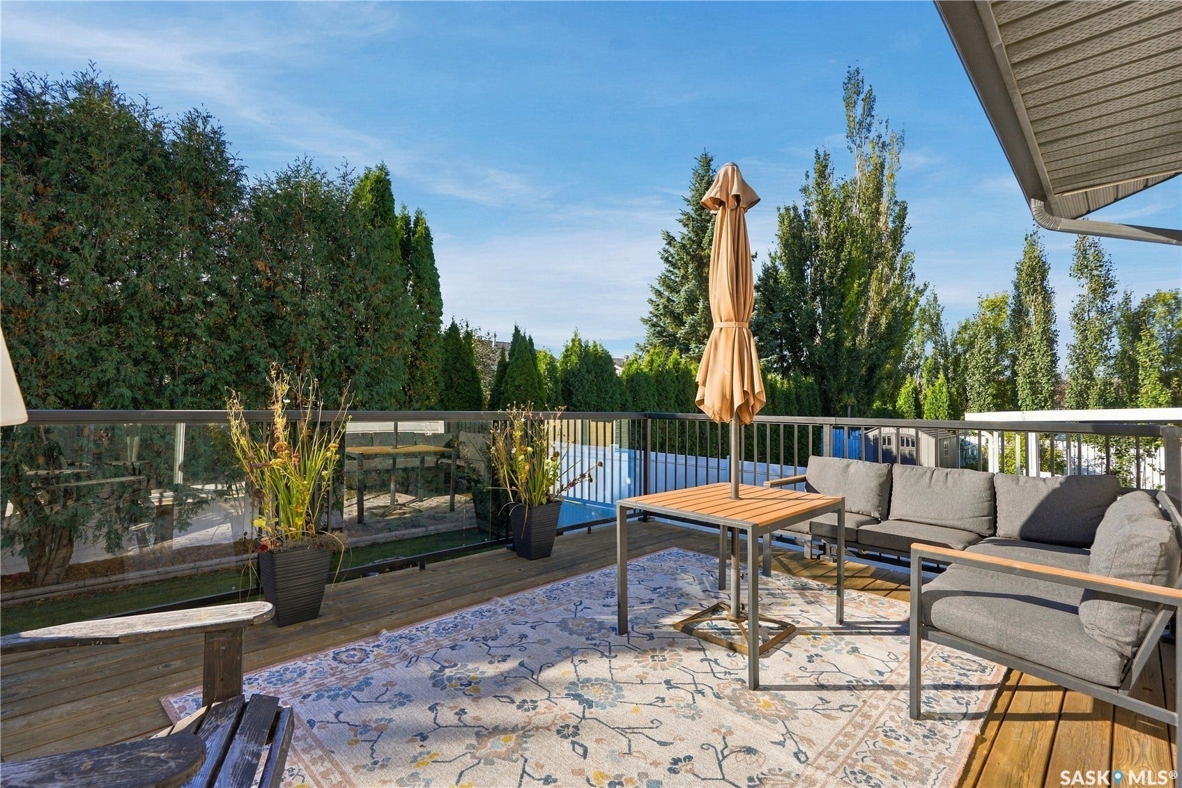 Expansive deck featuring wood decking, glass panel railings, and mature perimeter trees