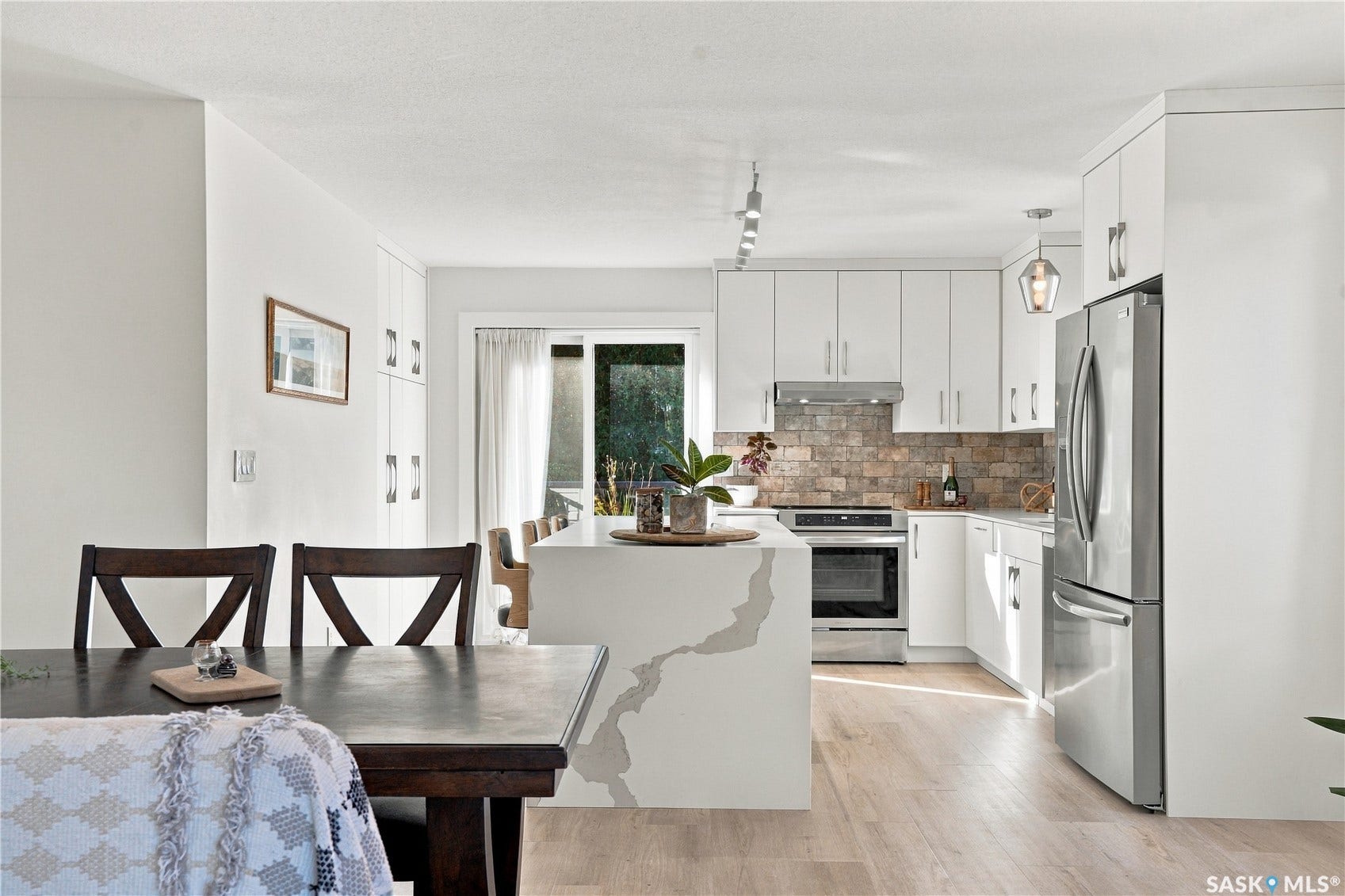 White shaker cabinetry, stainless steel appliances, a stone tile backsplash, a kitchen island with seating, and wood-finish flooring