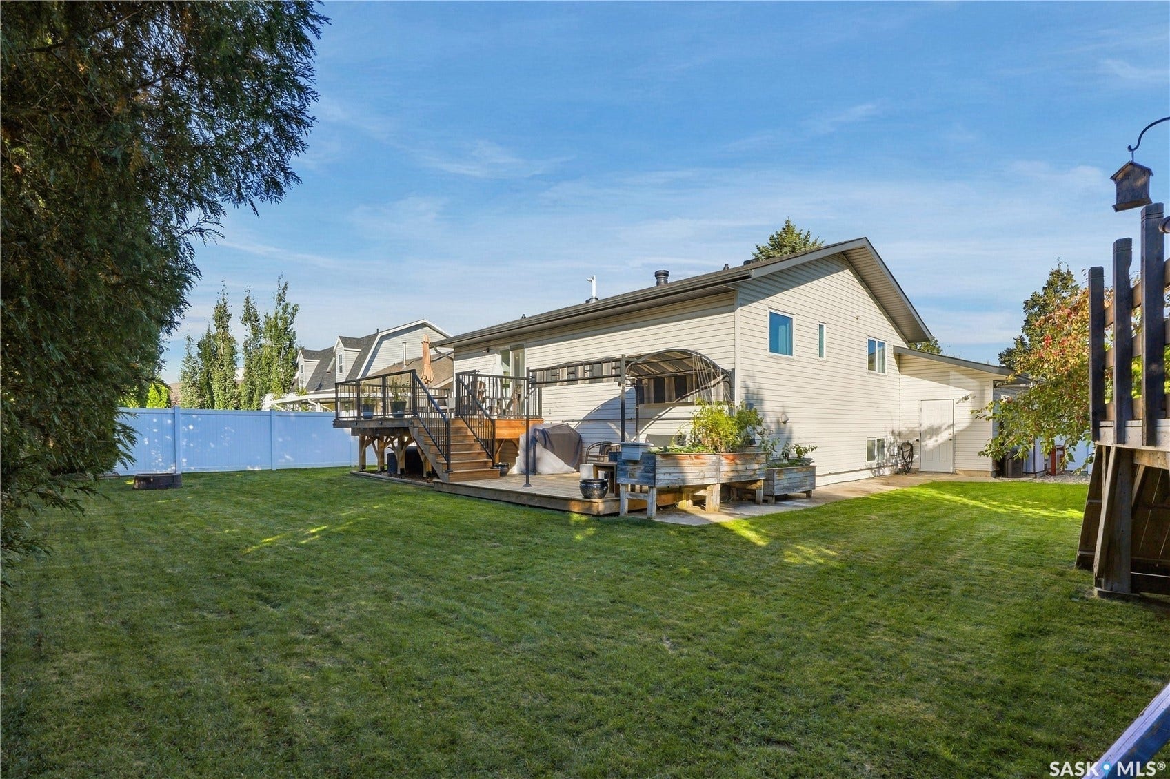 Expansive grass lawn with a multi-level wood deck featuring black railing and a partial overhead awning