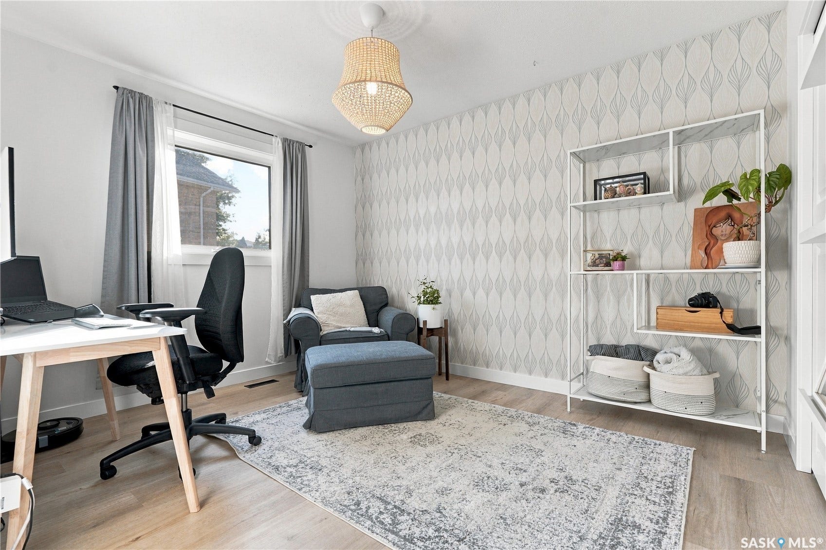 Wood-finish flooring, accent wall with patterned wallpaper, built-in shelving, ceiling-mounted light fixture, and window with dark curtain rod