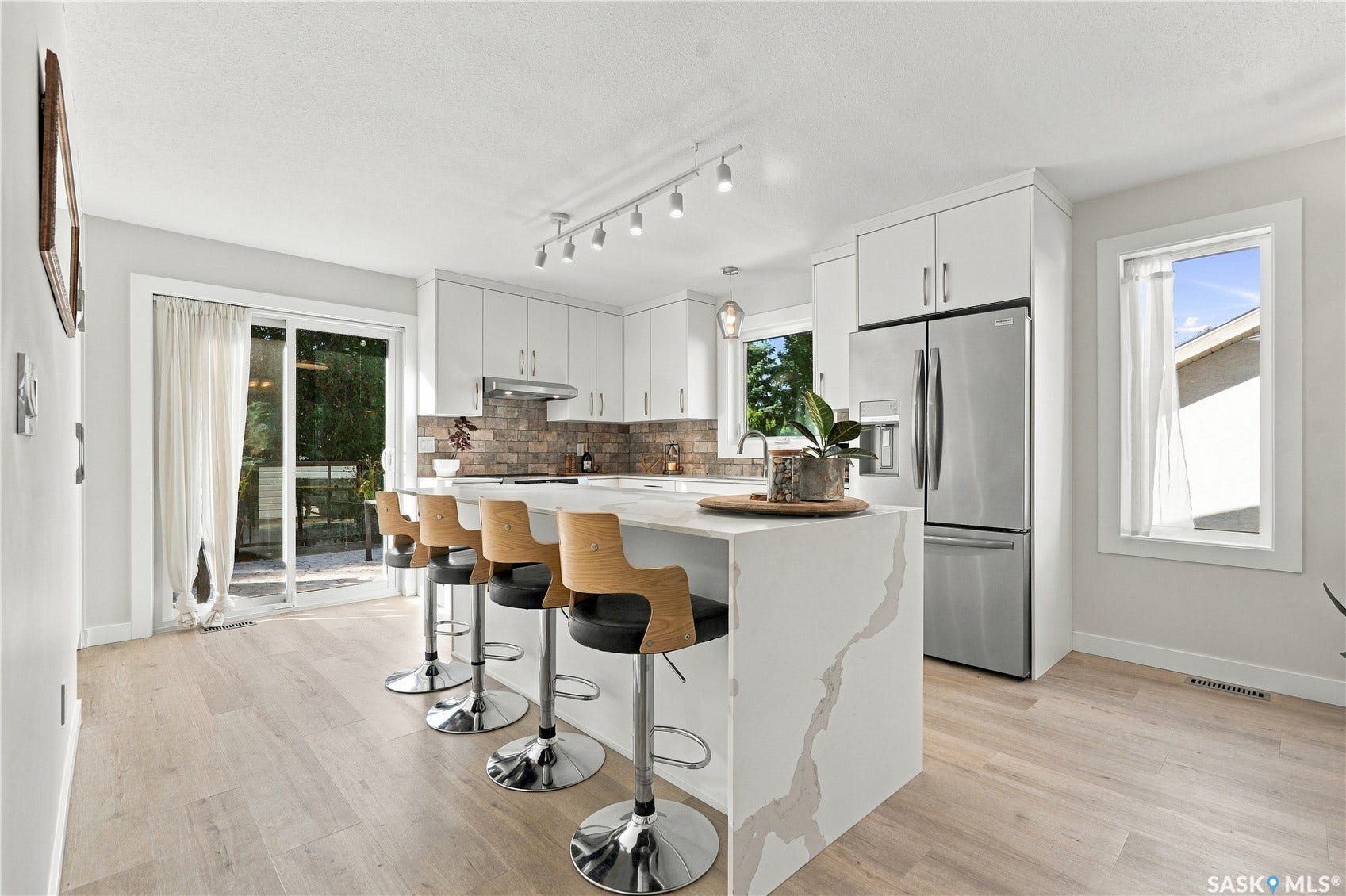 Modern kitchen featuring white cabinetry, stainless steel appliances, a center island with waterfall countertop, wood-finish flooring, and sliding glass doors