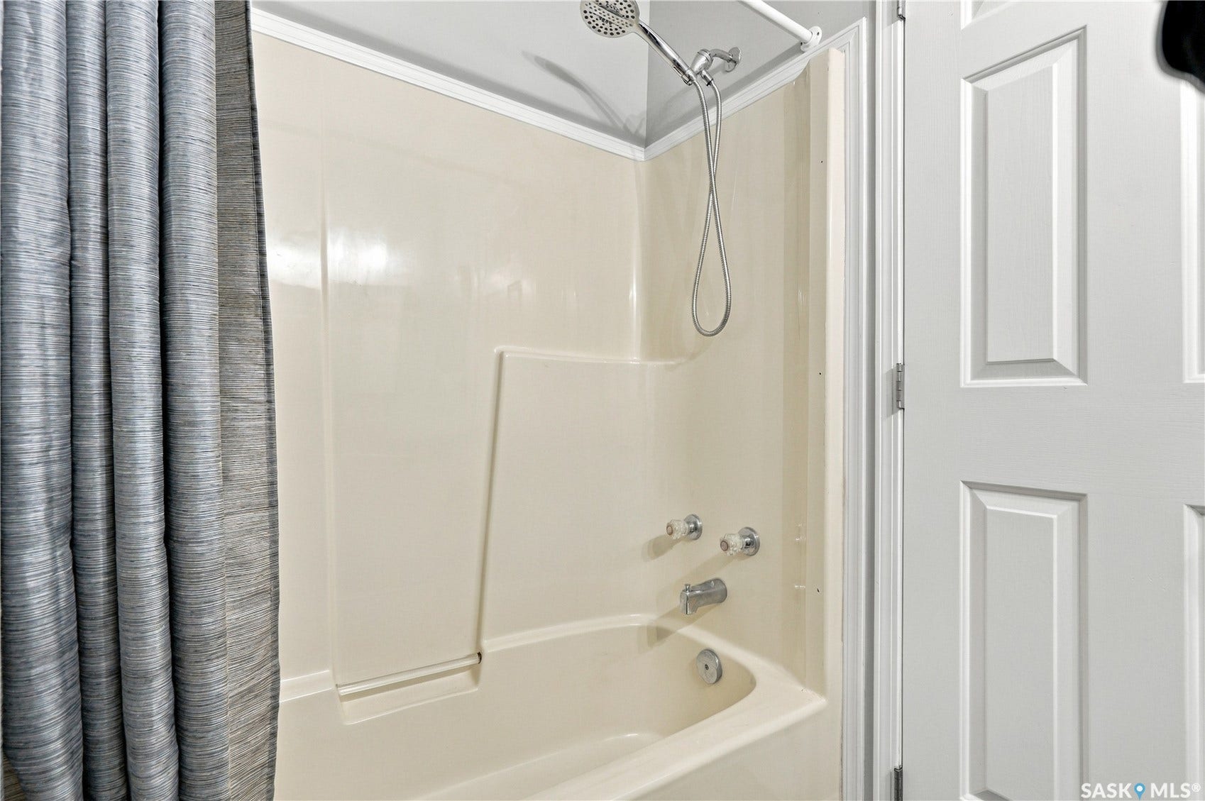 Bathtub and shower combination featuring a multi-function showerhead, integrated soap dish, and a white paneled door