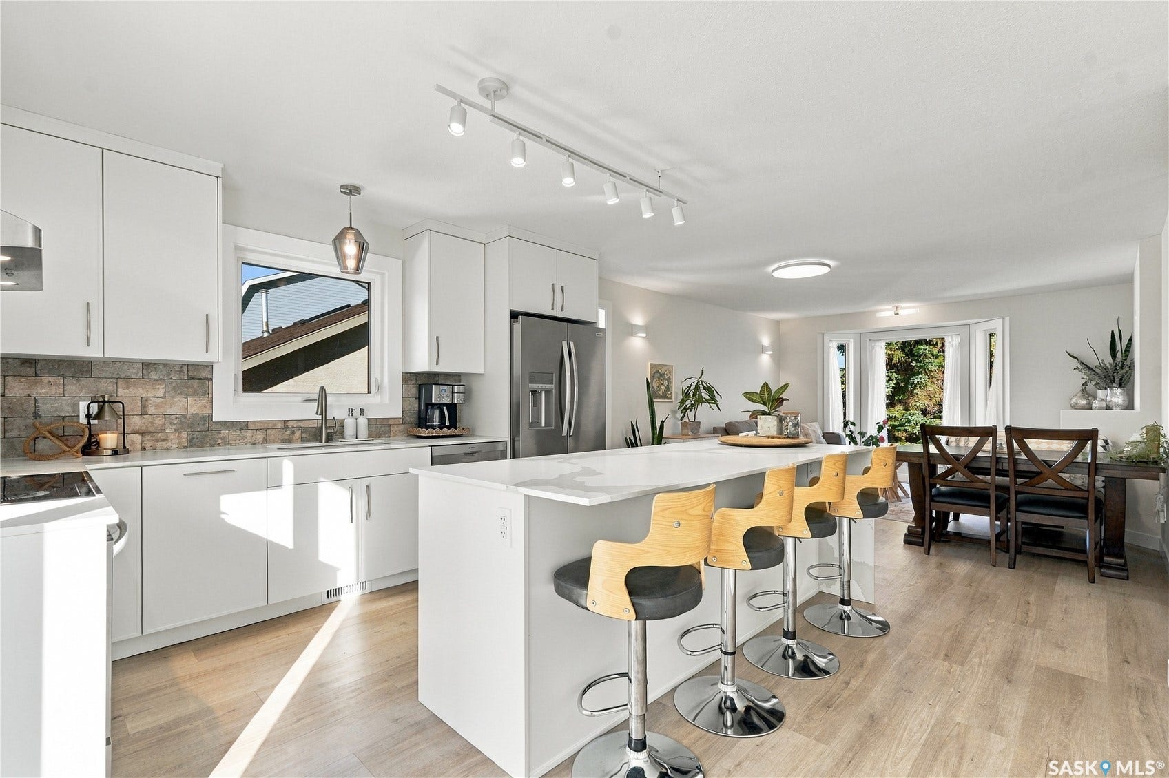 Bright kitchen with white cabinetry, stainless steel appliances, brick-style backsplash, and light wood-finish flooring