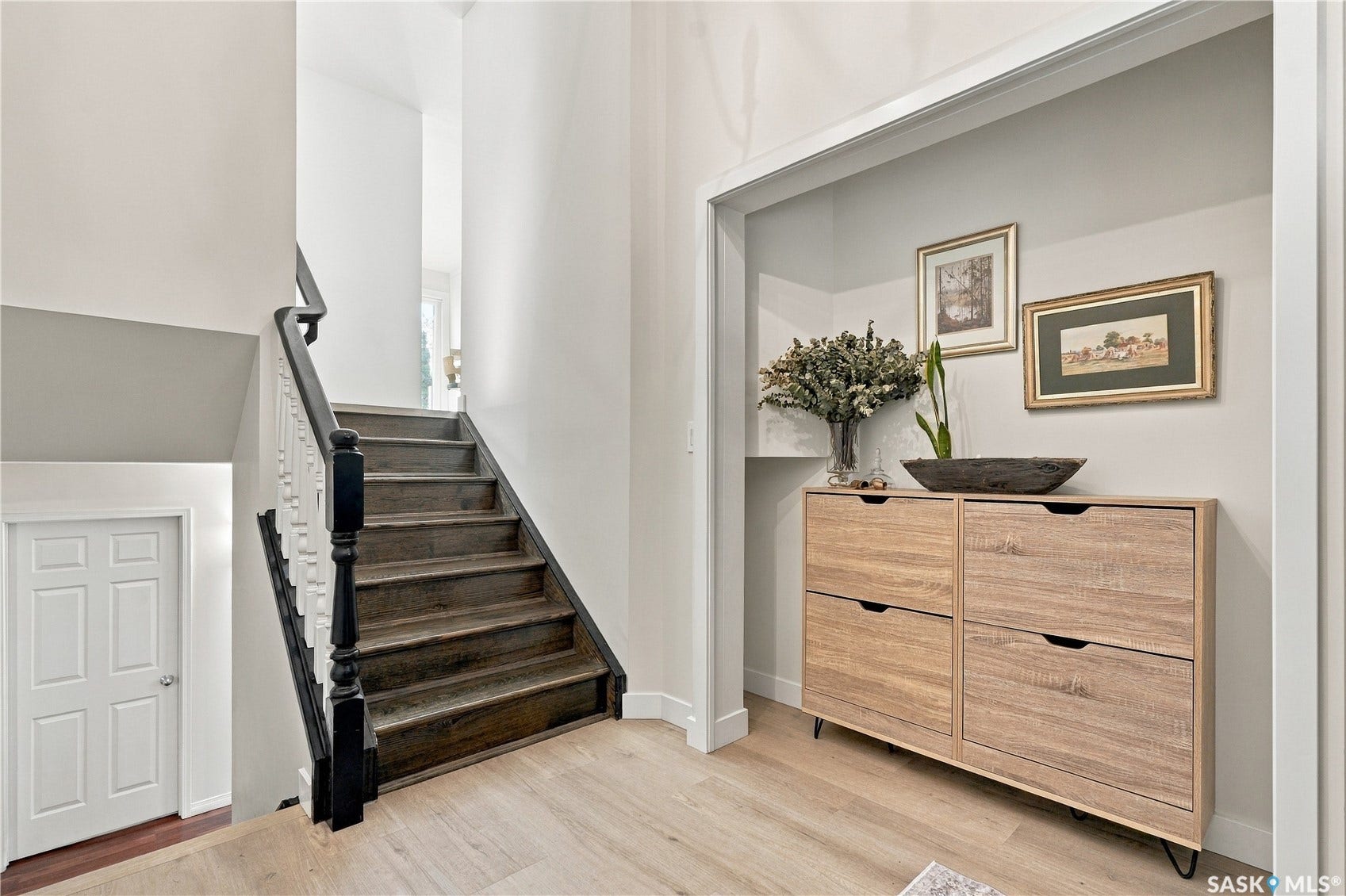 Hardwood stairs with painted risers and a dark wood handrail, light wood-finish flooring, and a recessed entryway