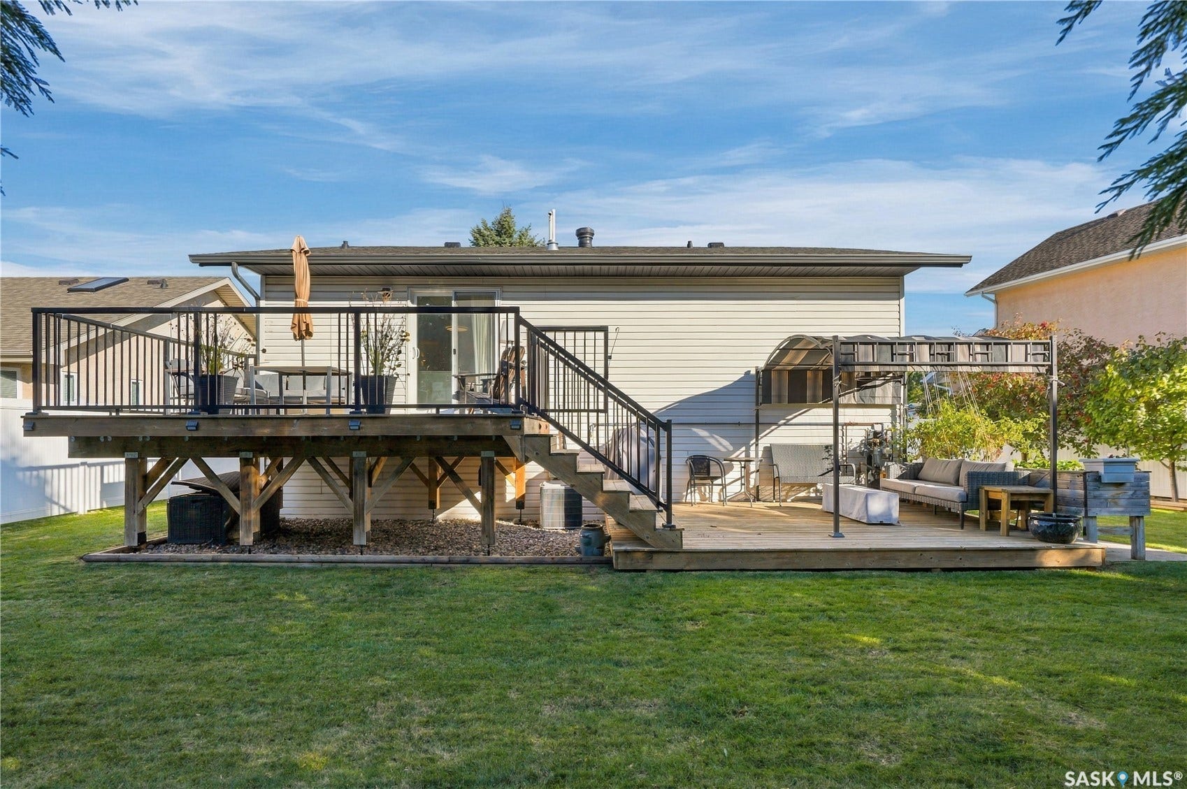 Expansive backyard featuring a manicured lawn, a raised wood deck with black metal railings, and a lower wood deck with a pergola structure