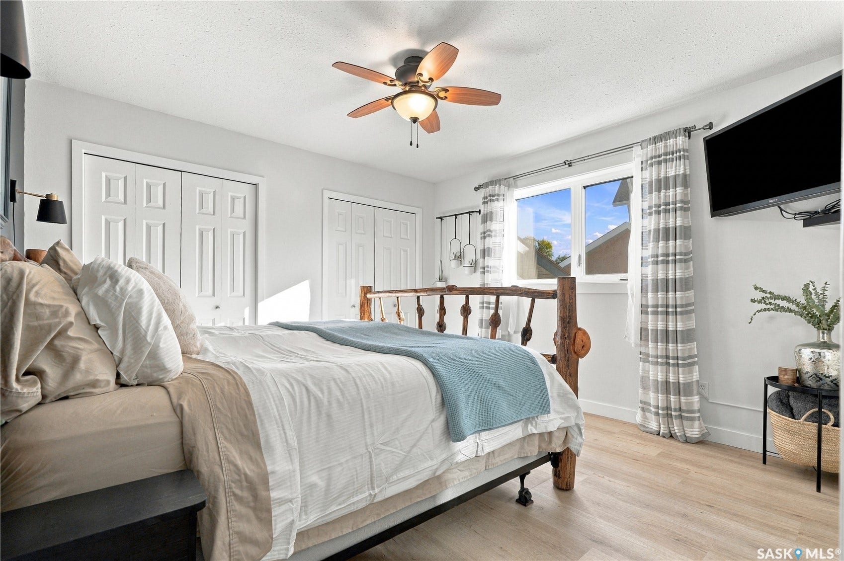 Wood-finish flooring, two sets of bi-fold closet doors, a ceiling fan with integrated lighting, and a large window with white trim