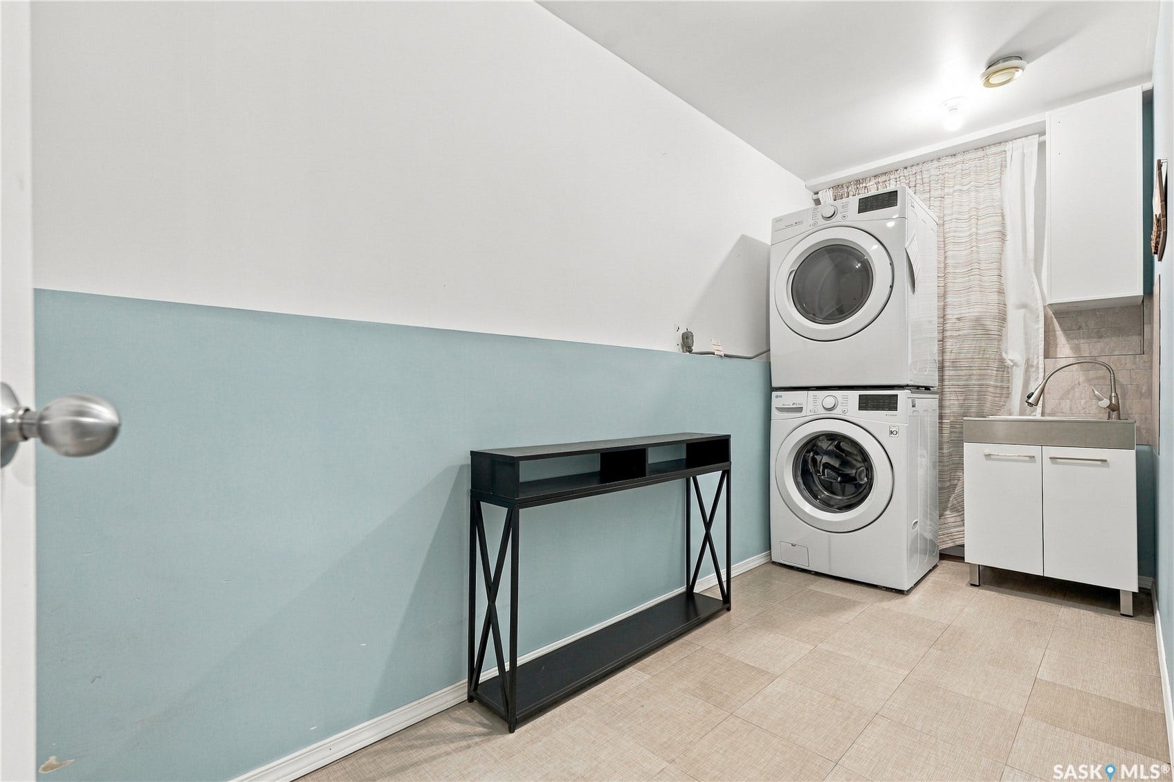 Laundry area featuring a stacked washer and dryer, utility sink with base cabinetry, and tiled flooring
