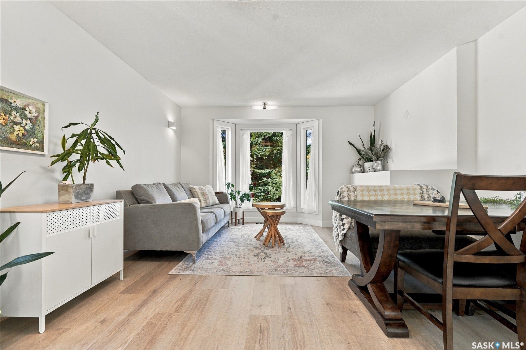 Light wood-finish flooring throughout, complemented by crisp white walls and a large bay window